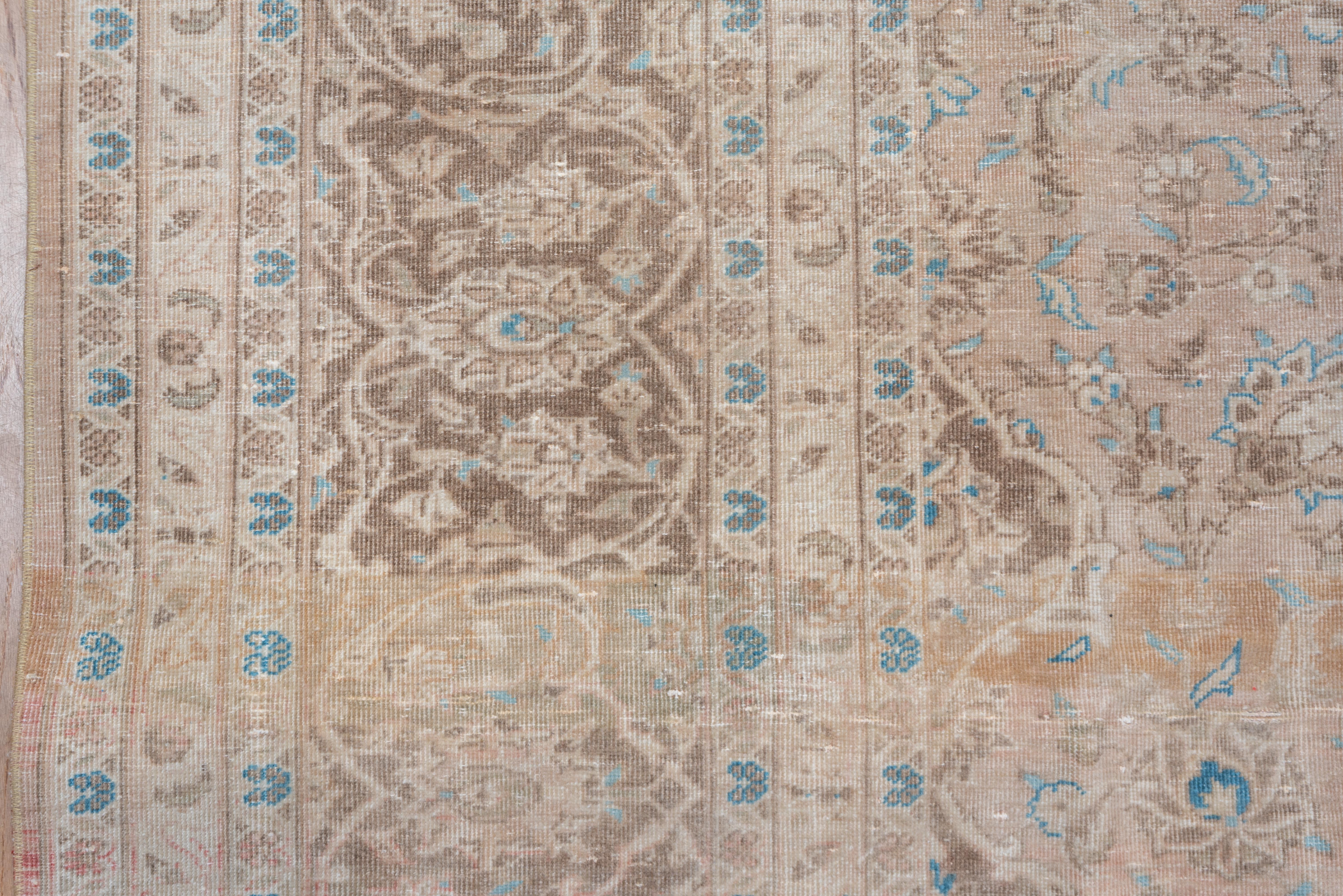 This Tabriz-style eastern Turkish medallion carpet shows a layered red-brown, cream and mid-blue medallion on an abrashed buff-tan palmettte decorated field, within an abrashed palmette, double vine and split arabesque design border.