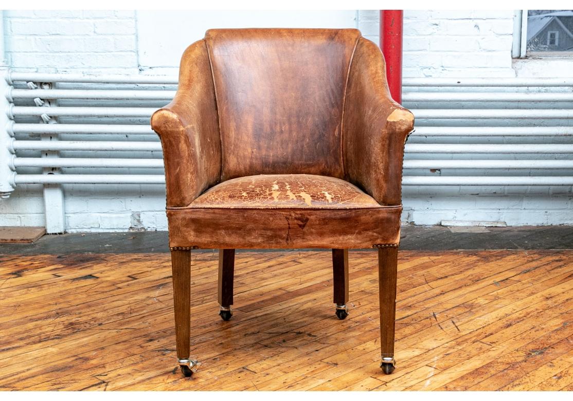 A fine antique leather library chair. In classic form with custom added casters, tapered legs and having a very desirable time worn appeal. Losses and expected wear to the leather. 
Measures 22” deep by 26” wide by 36” high. 
Please see photos for