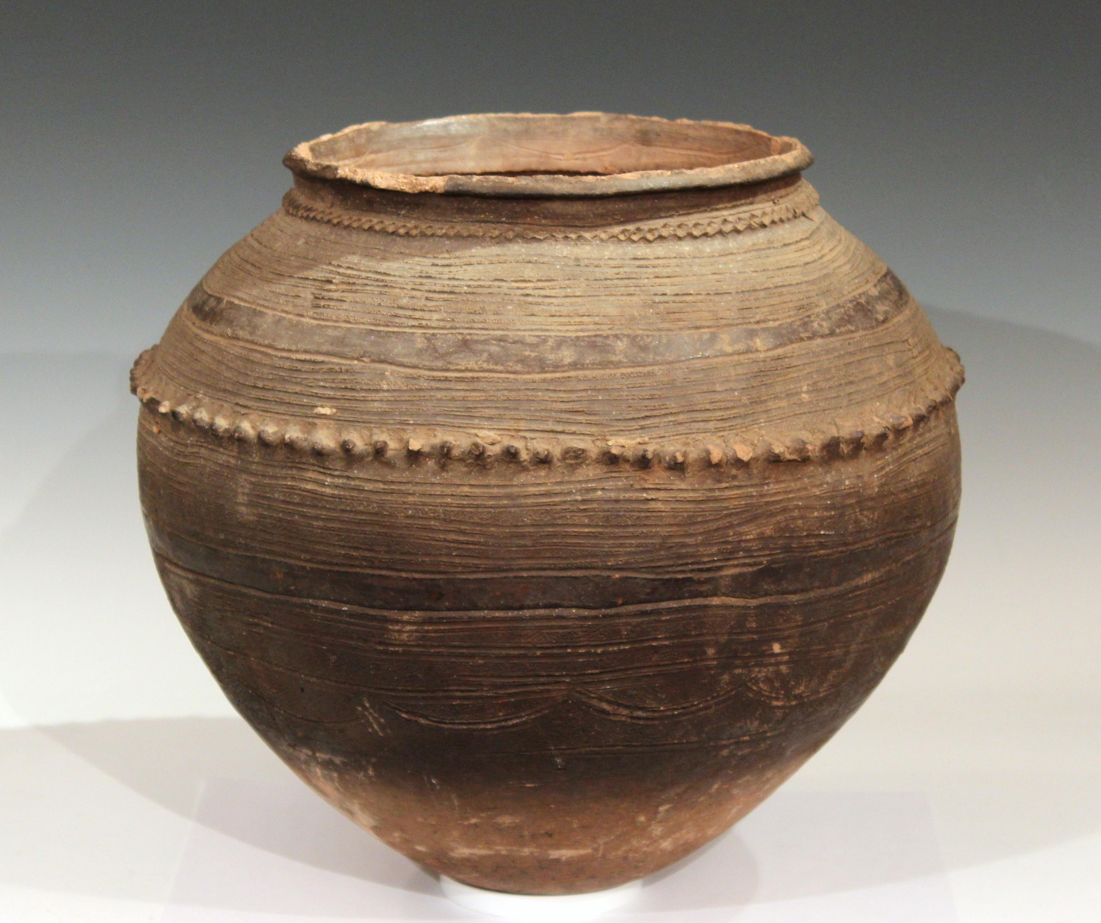 Big old Nigerian coiled terracotta round bottomed storage jar decorated all-over with incised horizontal bands and geometric designs and applied bands at the collar and shoulder, circa early to mid-20th century. Measures: 15