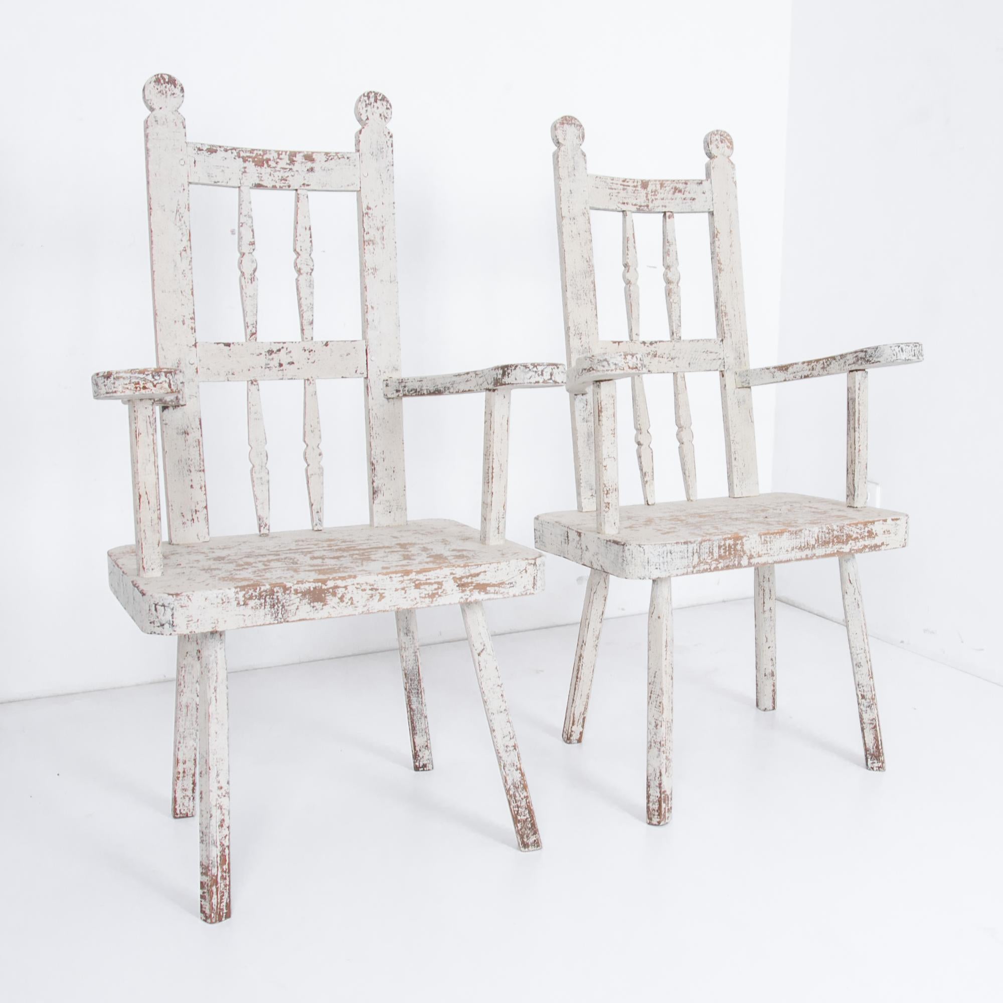 This pair of antique wooden armchairs was made in Northern Europe and exudes authenticity and warmth. The white paint has weathered beautifully into a charming patina, giving the rustic feel of a farmhouse. These armchairs rest on splayed legs, and