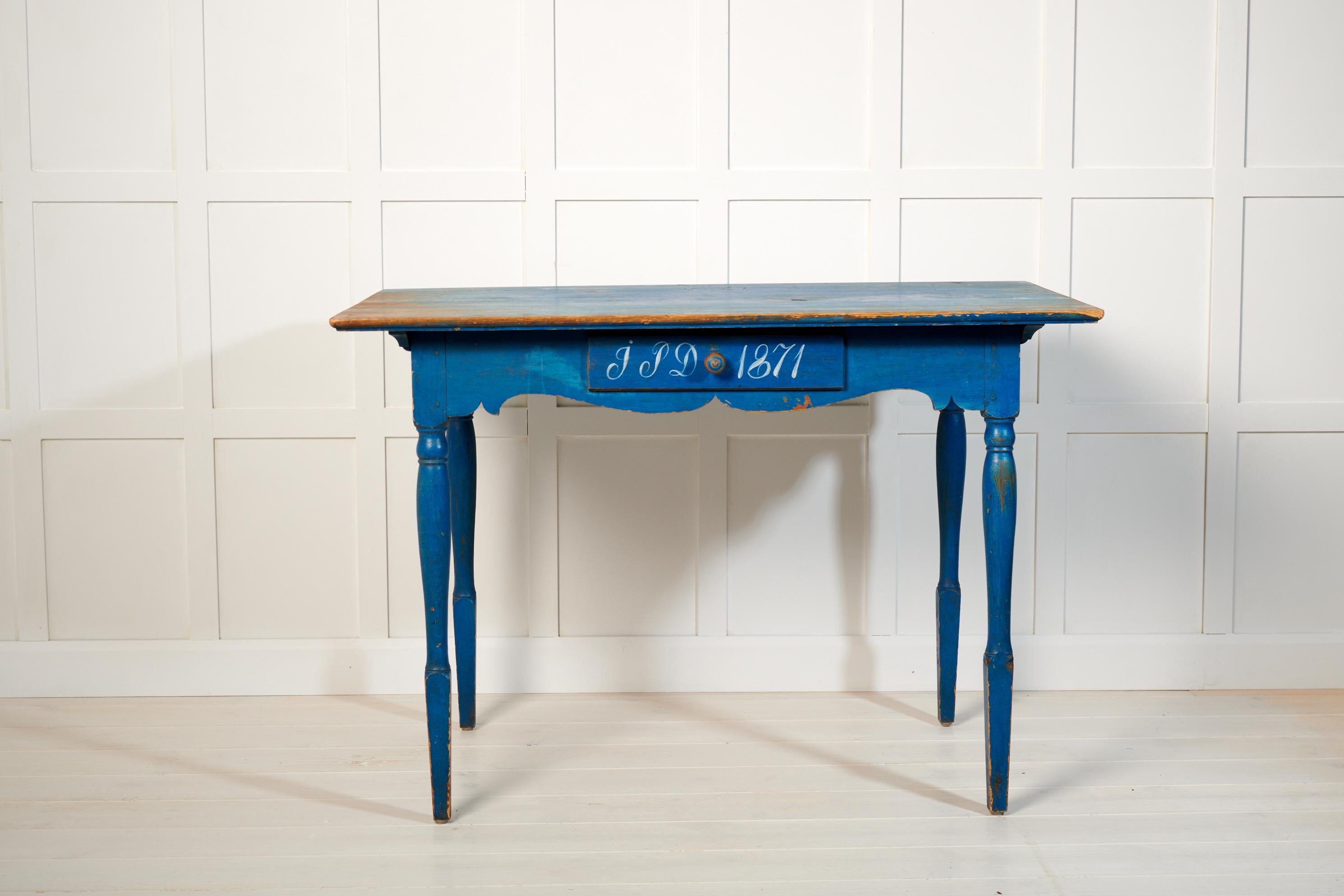 Antiker schwedischer Landhaustisch oder Schreibtisch mit einer Schublade. Der Tisch ist ein authentisches Landhausmöbel aus Nordschweden, handgefertigt aus massiver Kiefer. Der Tisch hat die ursprüngliche blaue Farbe mit aufgemalten Initialen und