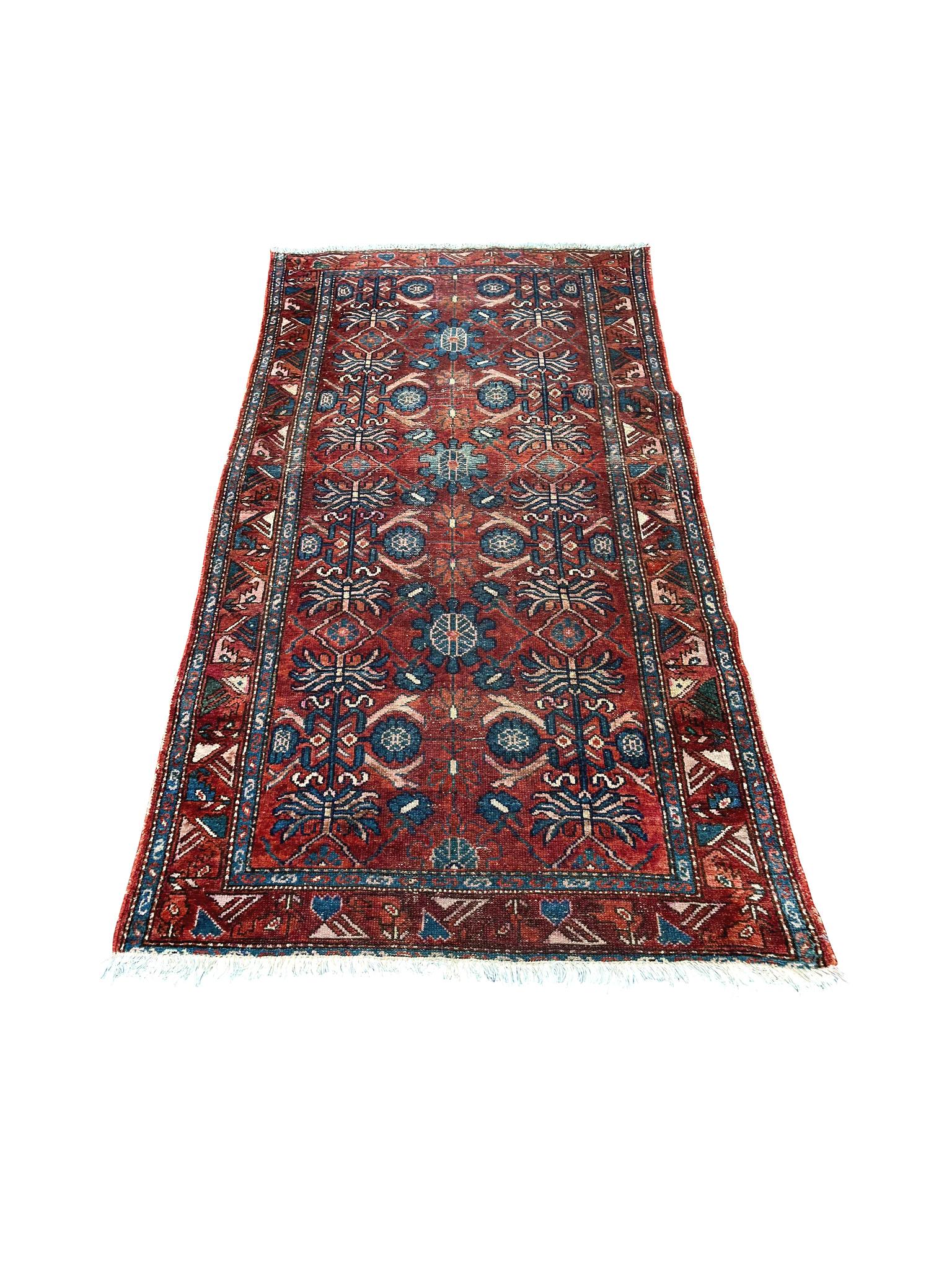 Hand-woven in the 1st quarter of the 20th Century, this beautifully aged Northwest Persian rug has a palette of red, blue, and ivory. The design centers 2 dark-blue floral columns in a red field surrounded by a series of borders of the same palette
