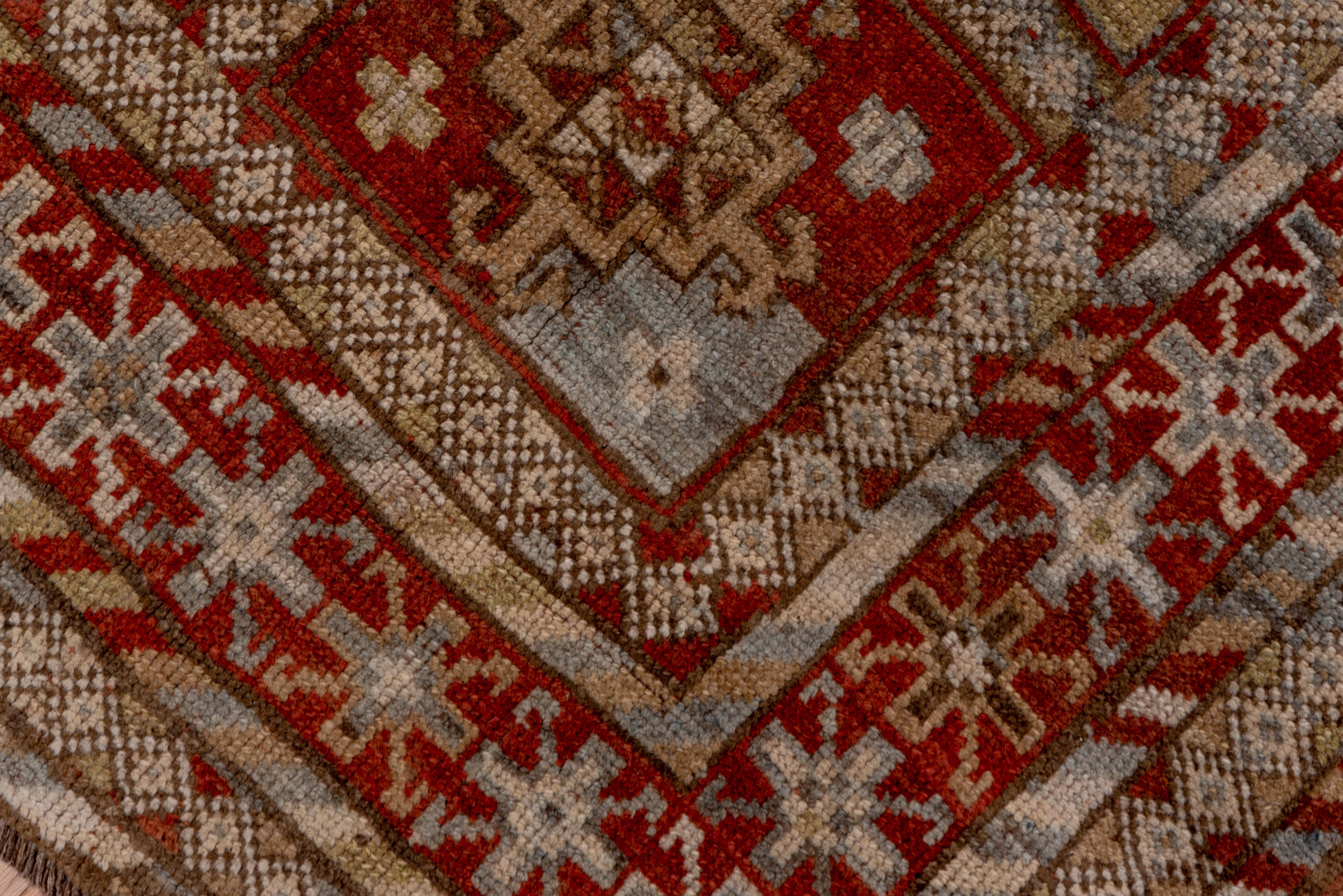 Ce tapis ancien du nord-ouest de la Perse présente une disposition tribale captivante, avec une grille de compartiments rectangulaires abritant chacun un médaillon géométrique stylisé. Tissé dans des tons chauds de terre cuite, de taupe, de camel et