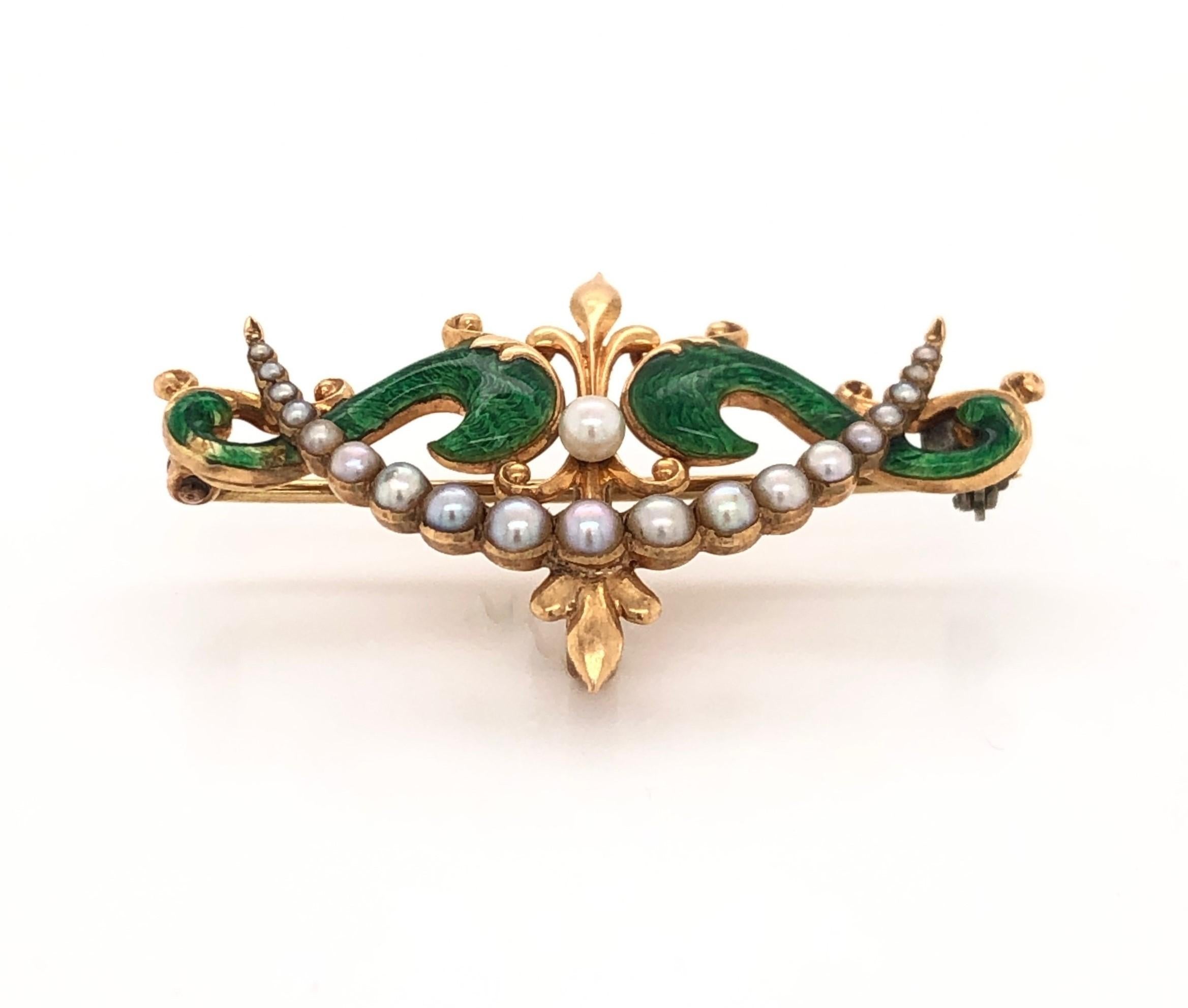 Petite and elegant with a scroll motif, this antique fourteen carat 14K yellow gold pin brooch is hand decorated with a vibrant green enamel and adorned with a crown of pearls. Measuring 1-1/2 inches wide and just under an inch top to bottom, it sit