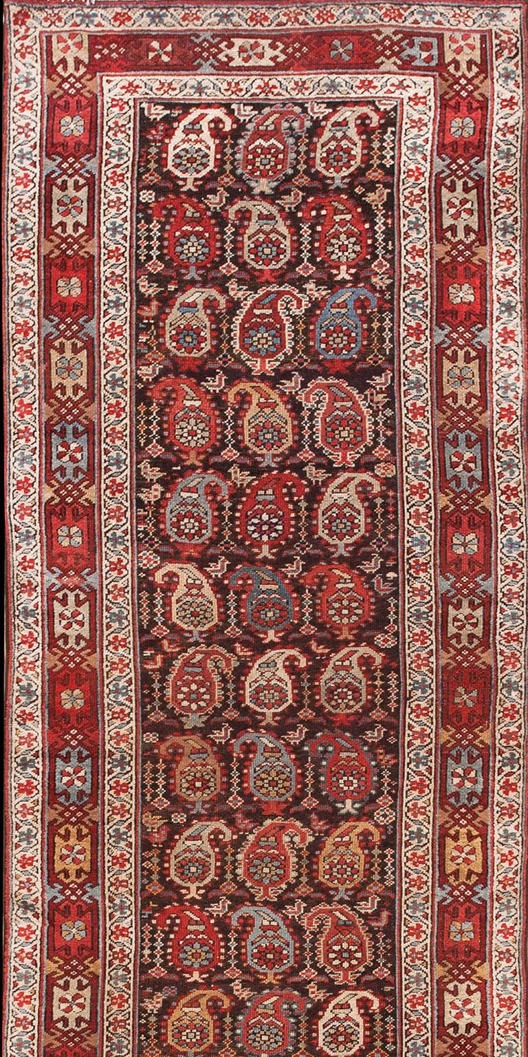  Allover-Muster mit Reihen von Boteh und kleinen Vögeln auf braunem Grund. Interessante Hauptbordüre mit verknüpften Designelementen auf einem alternierenden Farbhintergrund. Handgeknüpfte Wollkonstruktion.