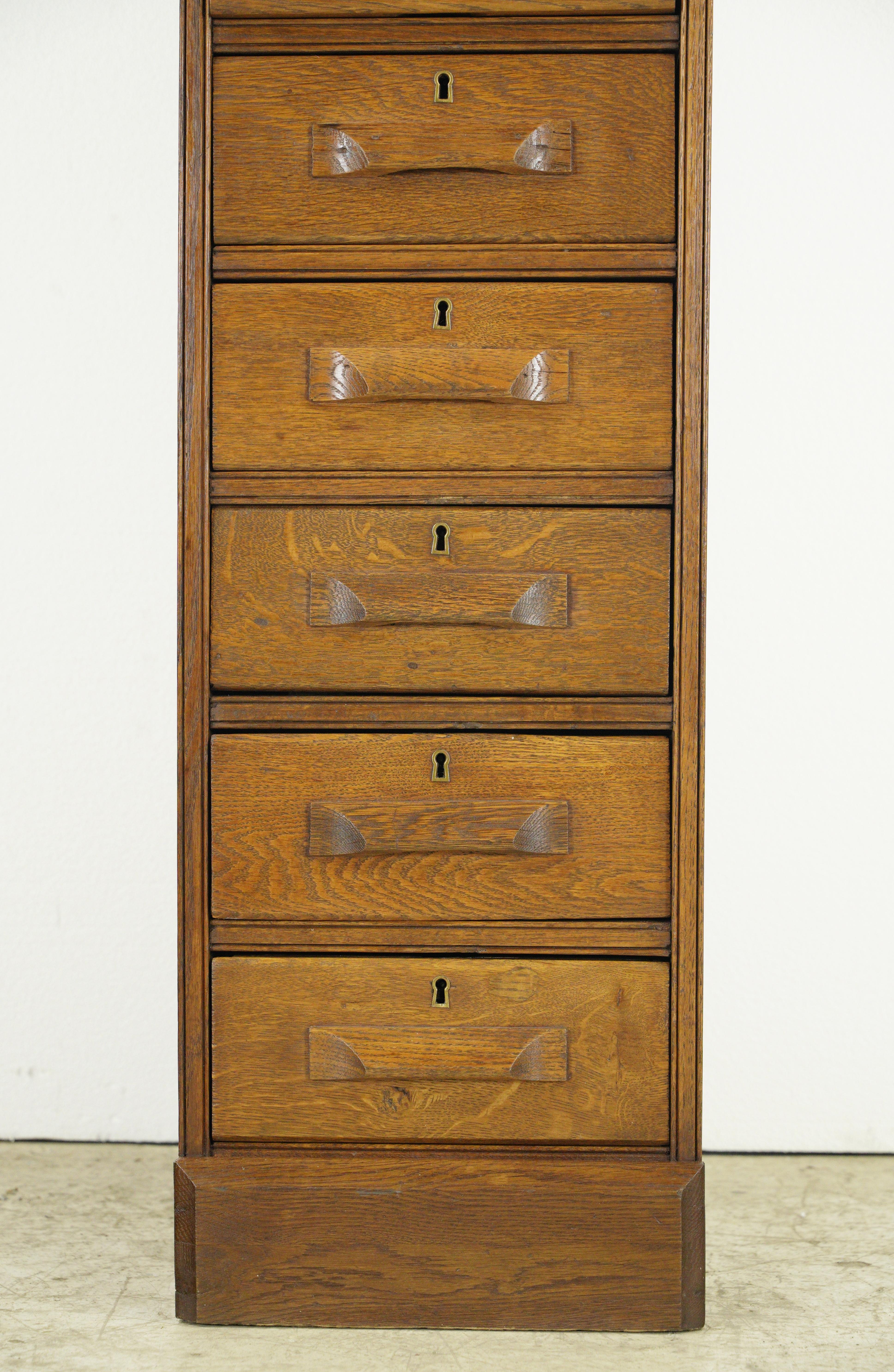 Dark tone oak filing cabinet with eight drawers with wooden pulls and brass keyhole hardware. Good condition with appropriate wear from age, with a minor split in the top. One available. Please note, this item is located in one of our NYC locations.