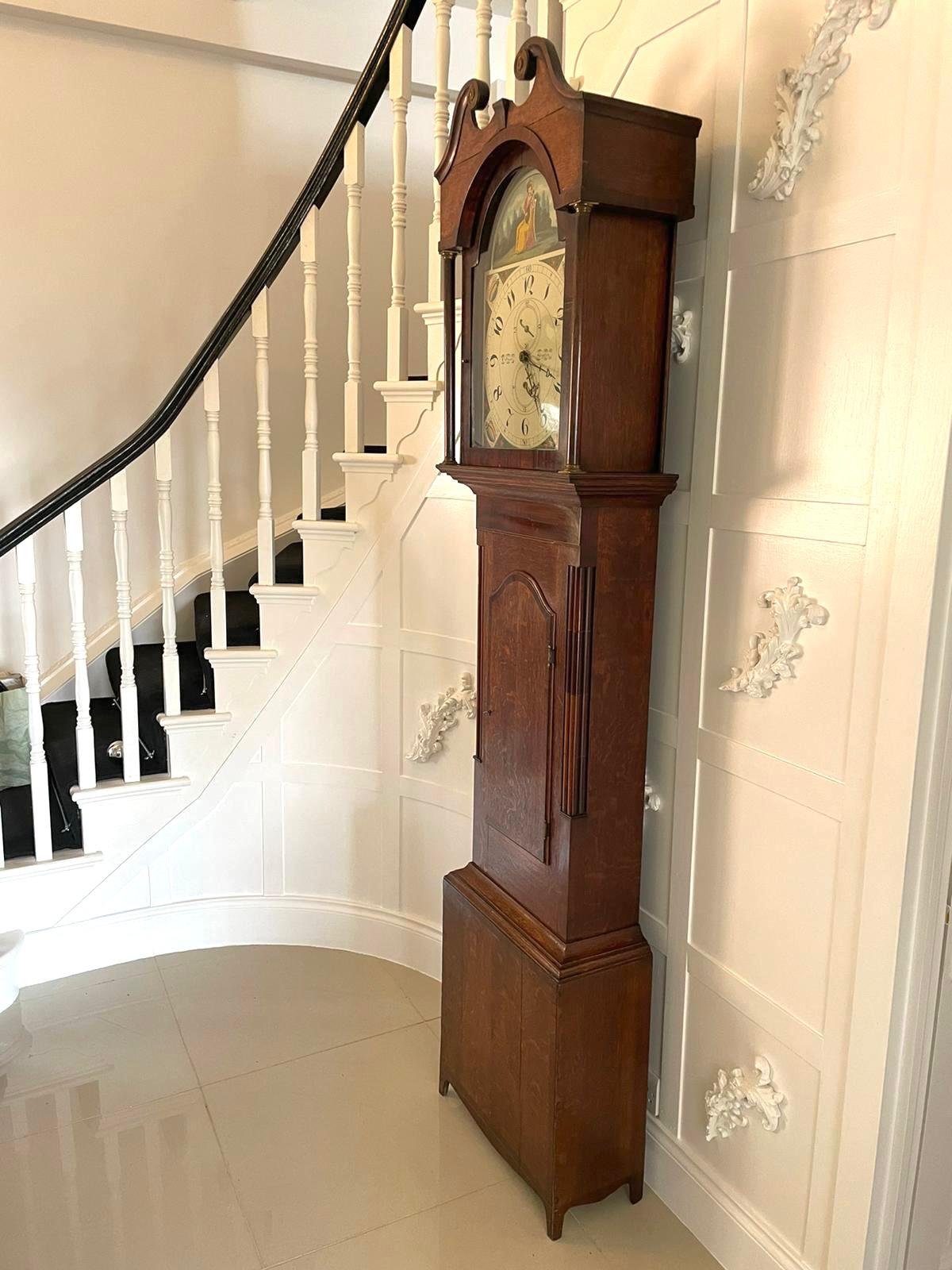 An antique oak and mahogany grandfather clock by W Prior, Skipton with a swan-neck pediment and an attractively decorative arched painted dial with a date and seconds dial. It has a 30 hour movement striking with a bell on the hour. The lovely oak