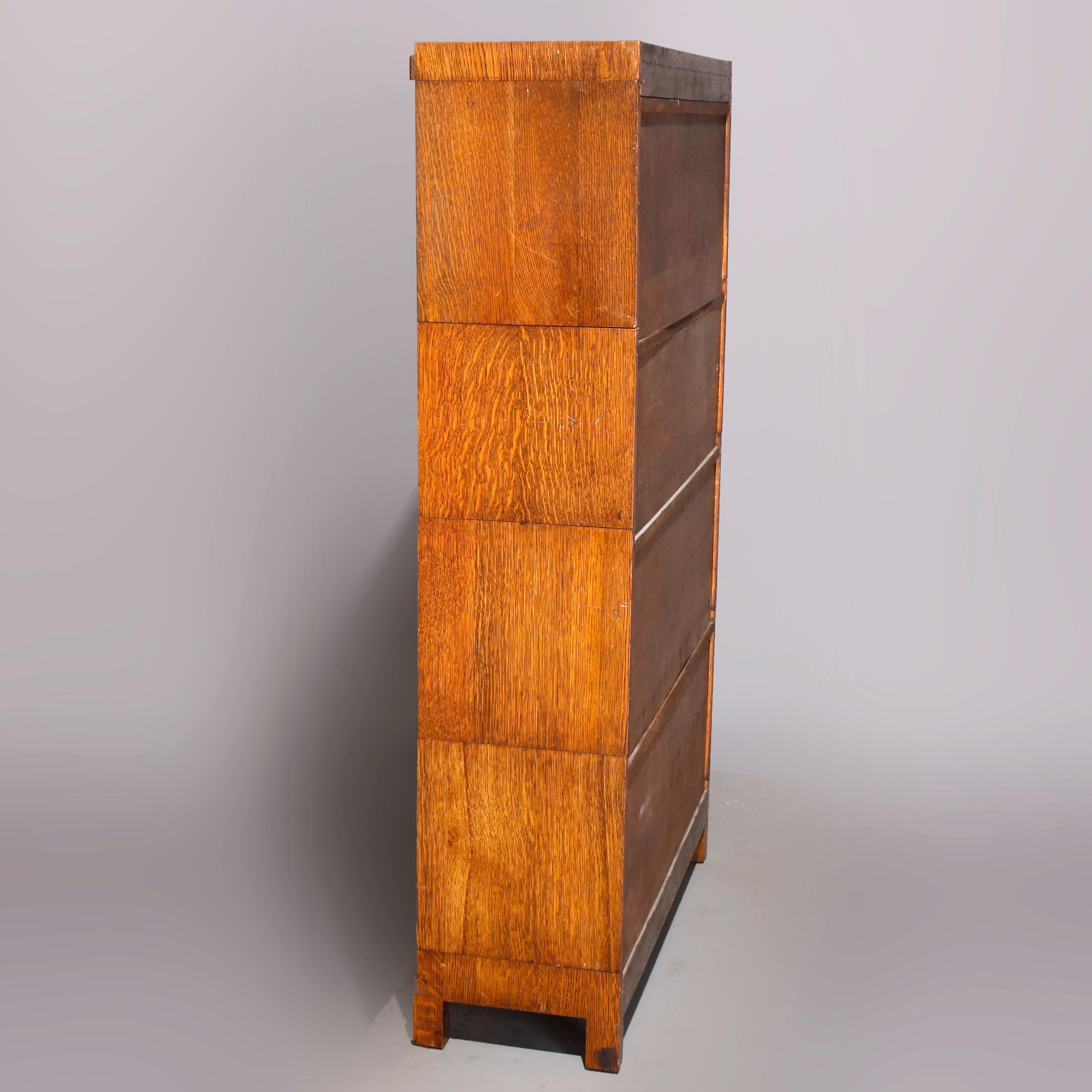 An Arts & Crafts sectional Barrister bookcase in the manner of Globe-Wernicke offers quarter sawn oak construction with four stacks having a pull-down glass door surmounted by removable crown and raised on square and straight legs, circa