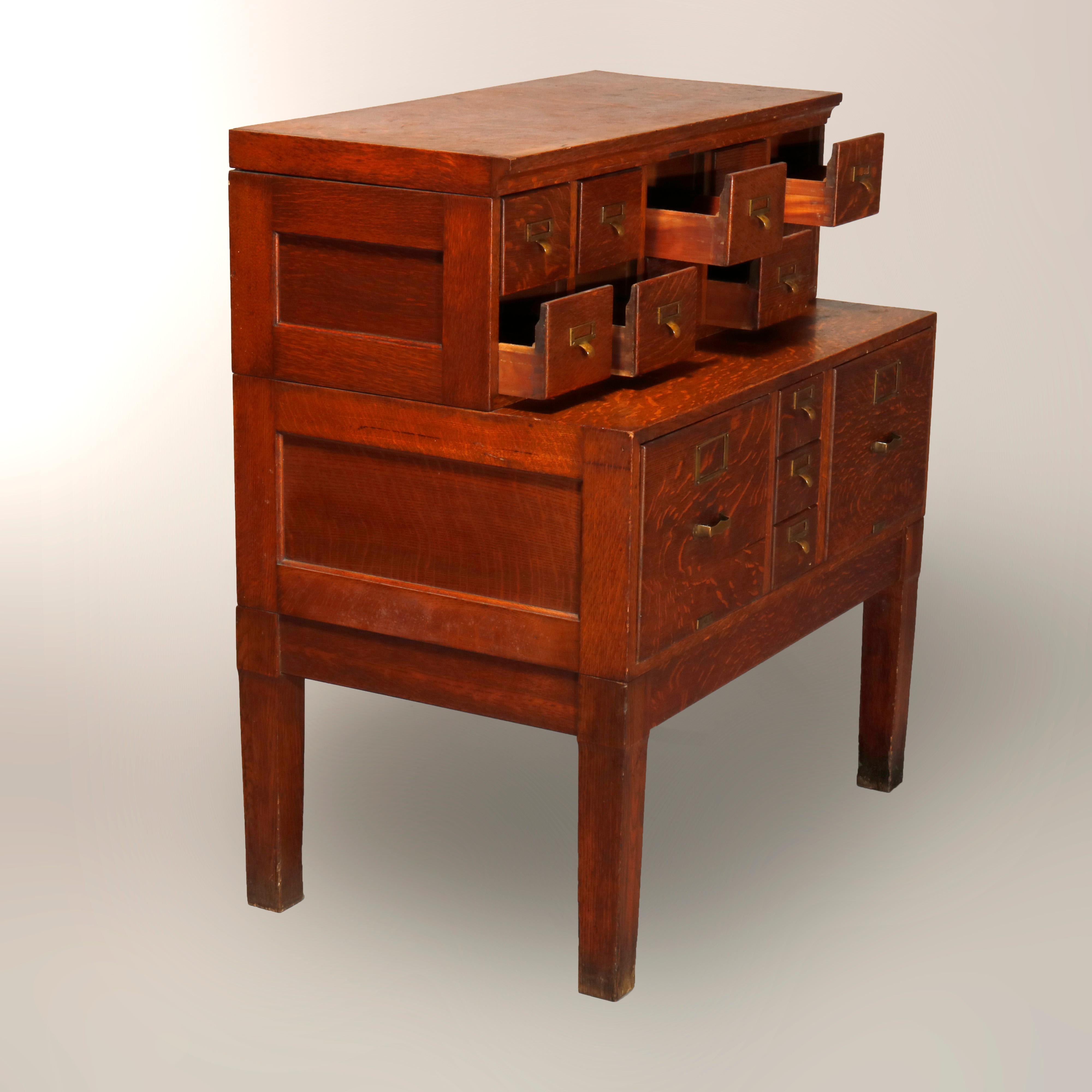 An antique Arts & Crafts library research card catalog filing cabinet offers paneled oak construction with stacked units having an upper with ten small drawers and lower with centra tower of three smaller drawers flanked by standard fining drawers,