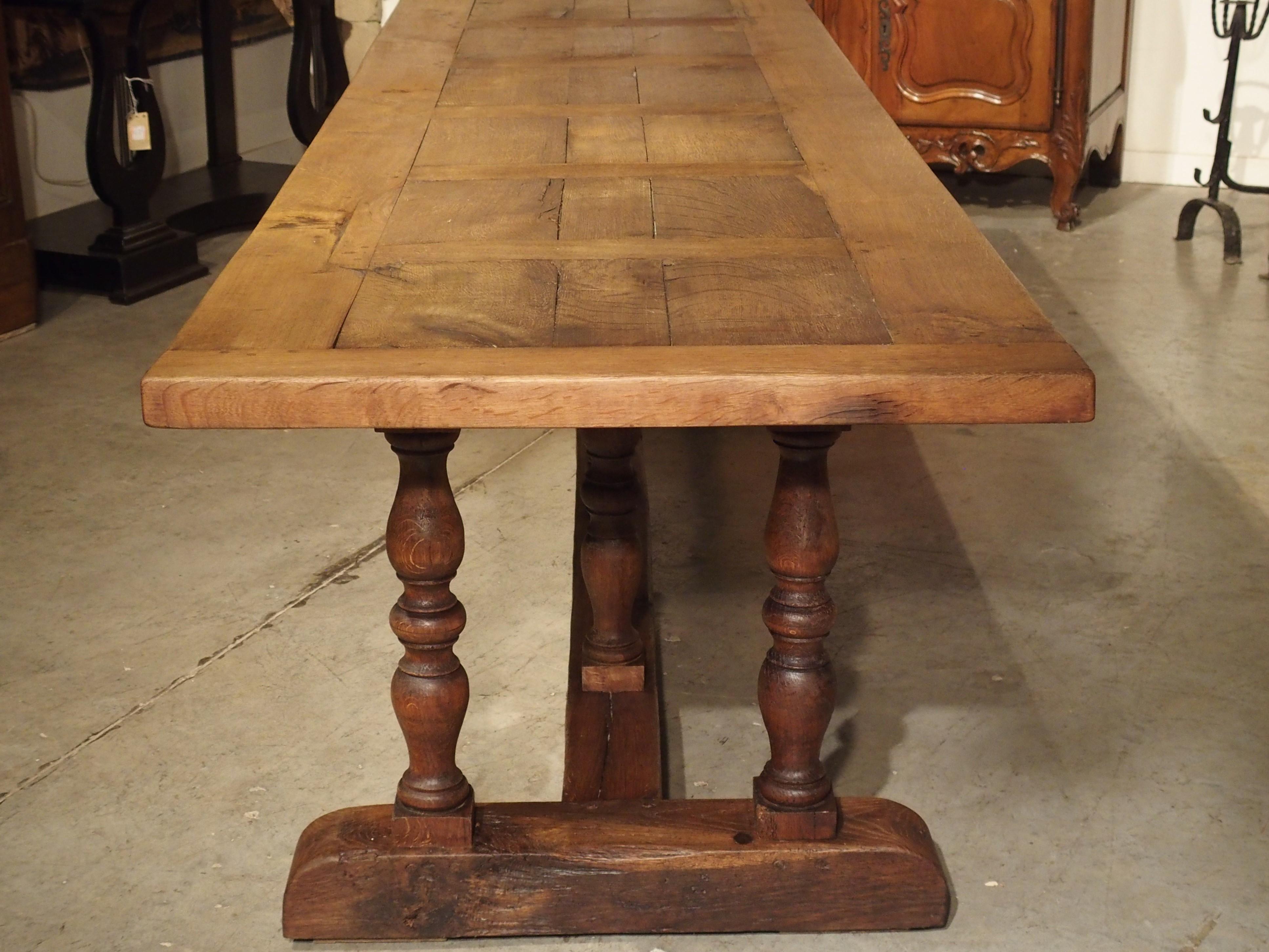 This antique French dining table is constructed of oak and was made in the mid-1800s, probably used in an elegant French Mas. The long top is supported by 2 balusters at each end and 3 balusters along the center beam stretcher. The legs at either