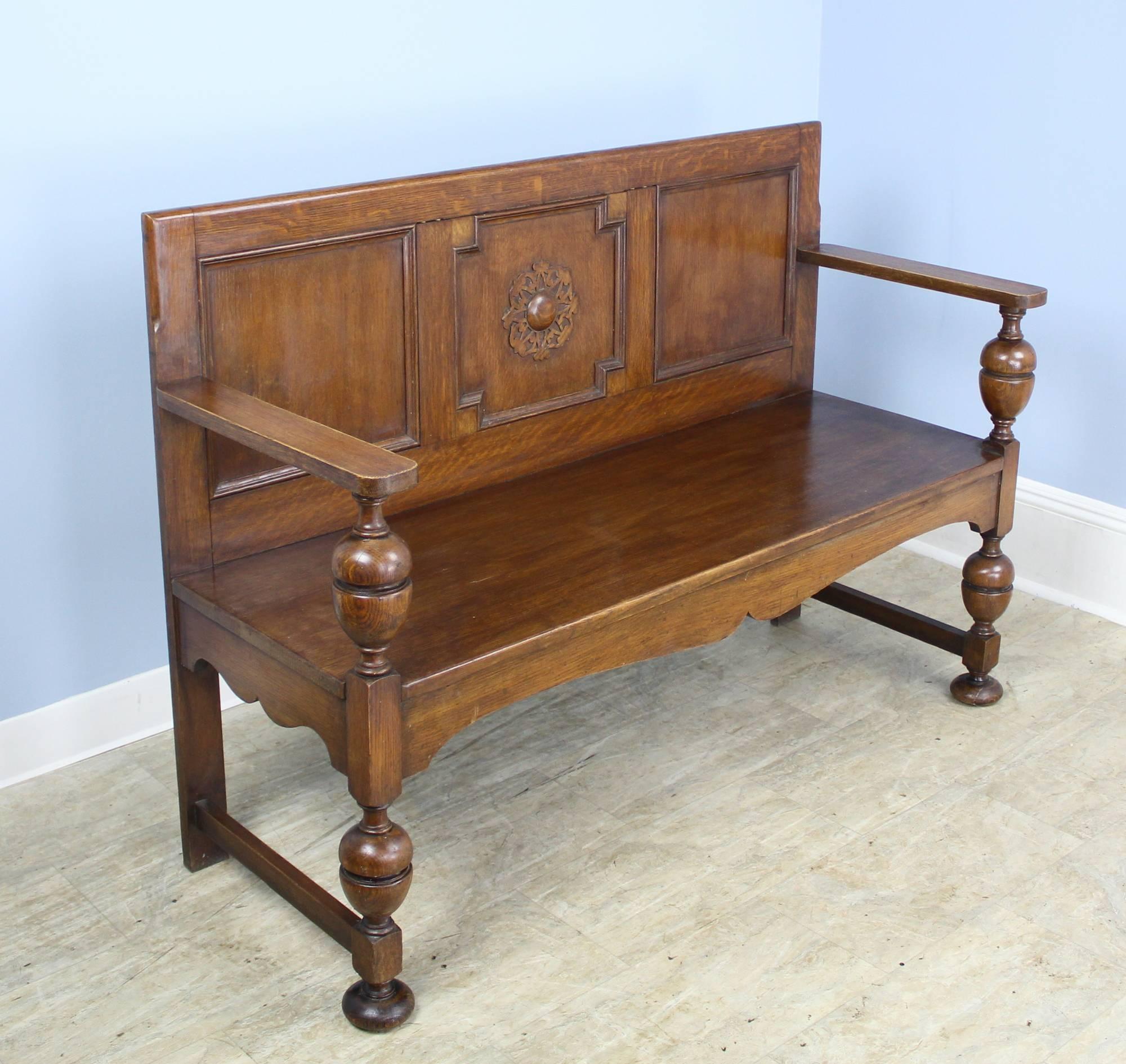 A handsome oak bench with a three panelled back featuring a carved medallion. Turned arms and legs with charming ball feet. Good seat height. Could be made an inch higher with a gusseted cushion.