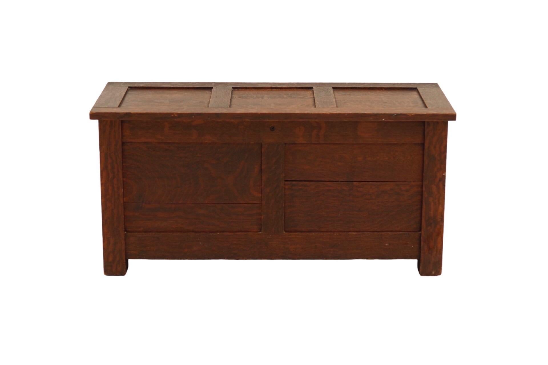 An arts and crafts period blanket chest made of oak, stained in a mahogany brown. The lid with three panels is hinged and opens revealing a lift out tray made of pine, with more storage below.
