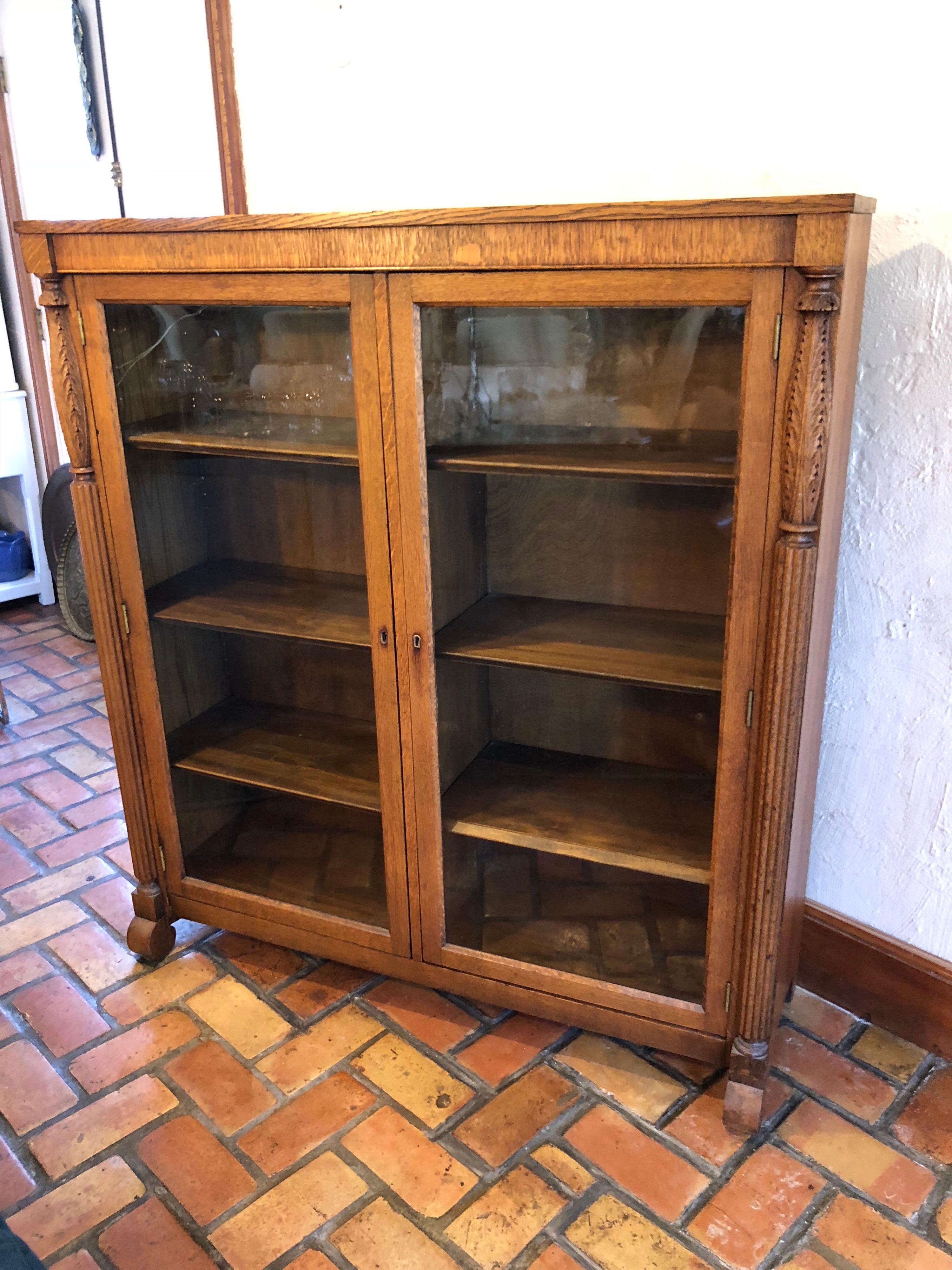 Antique oak bookcase with original keys. Nice quarter sawn oak grain woodwork with carved ,channeled columns adorned with acanthus leaf style. Four adjustable solid wooden shelves on both sides. Original keys to lock doors for safekeeping your