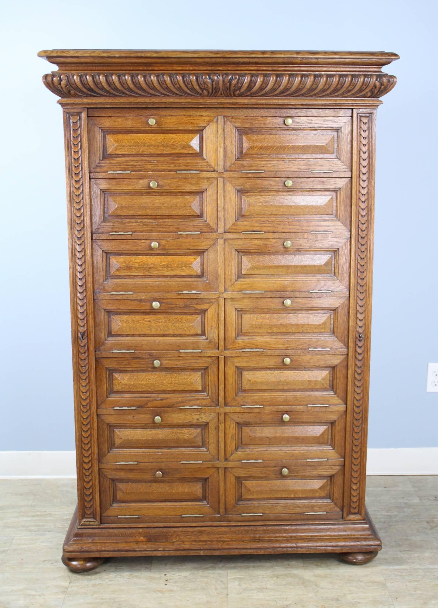 An ornately carved French oak cabinet in the Wellington style, with closures on each side to lock and secure the 14 compartments shut. The cornice has a spectacular pattern which is echoed on the side closures. The oak on this piece is in very good