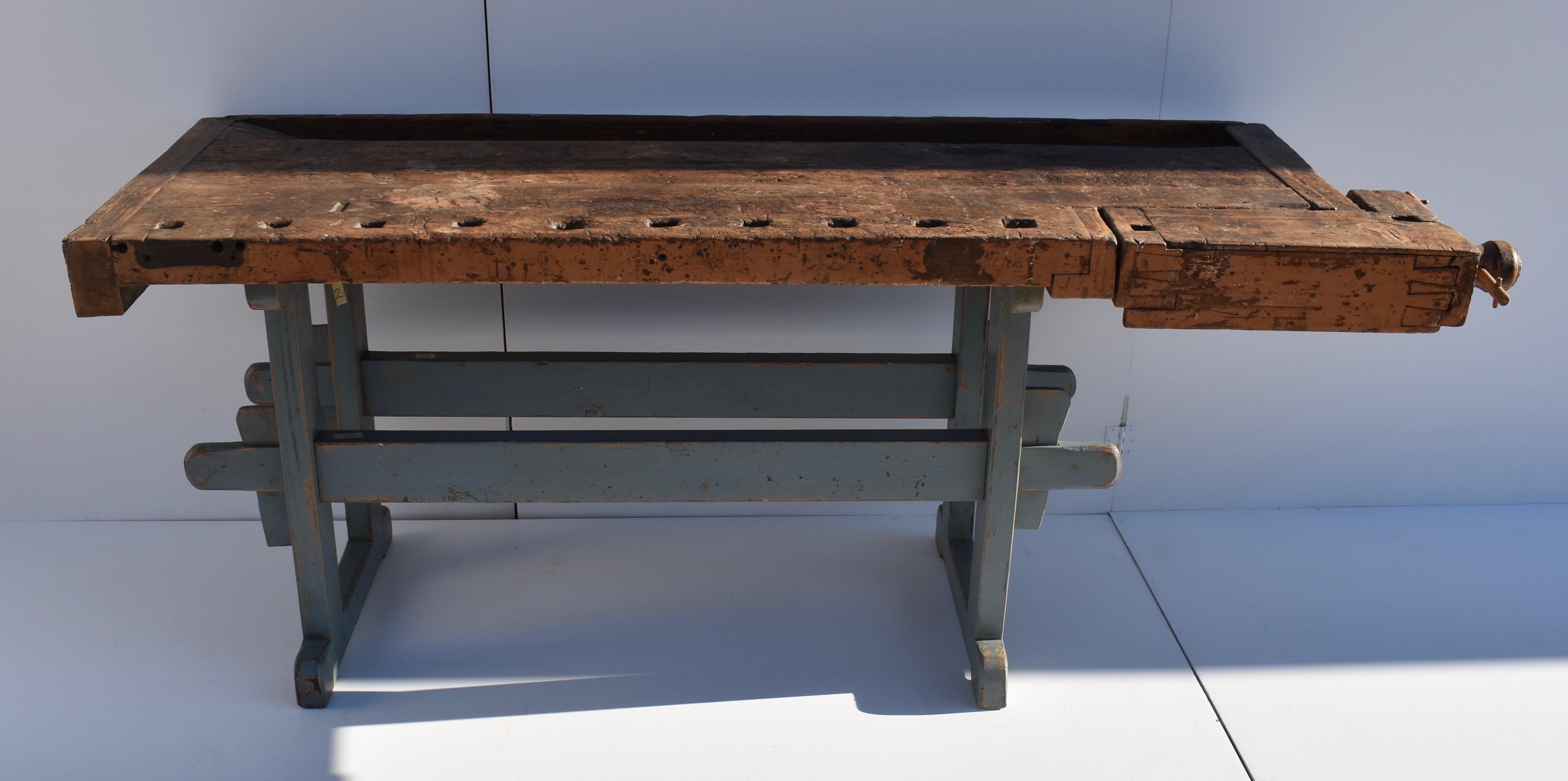 This magnificent oak carpenter’s workbench has a trestle-style base, painted blue, the ends made from handcut members, through-tenoned and pegged together, and pulled tight on two 2” x 4” stretchers, secured with wooden keys.The bench surface is a