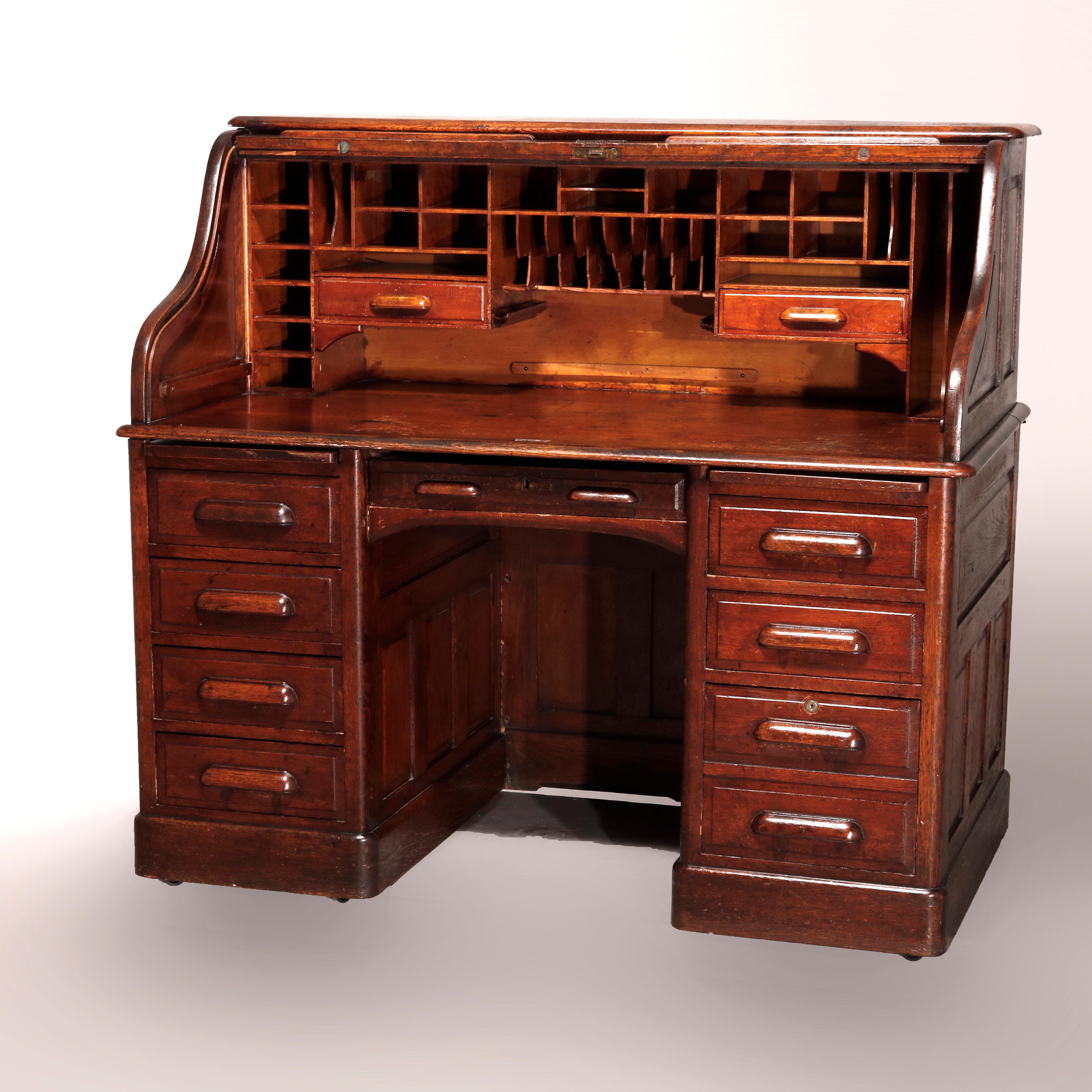 An antique desk in the manner of Derby offers quarter sawn oak construction with S-form roll top opening to interior pigeon holes and drawers over case with paneled sides and back, flanking drawer towers, foliate and cup handles throughout, circa