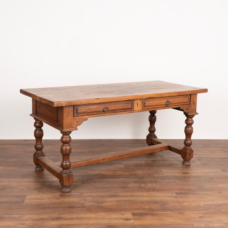 This attractive French oak writing table has two wide drawers in the apron and 4 turned legs connected by a low stretcher. Note that it is free-standing, with a handsome 