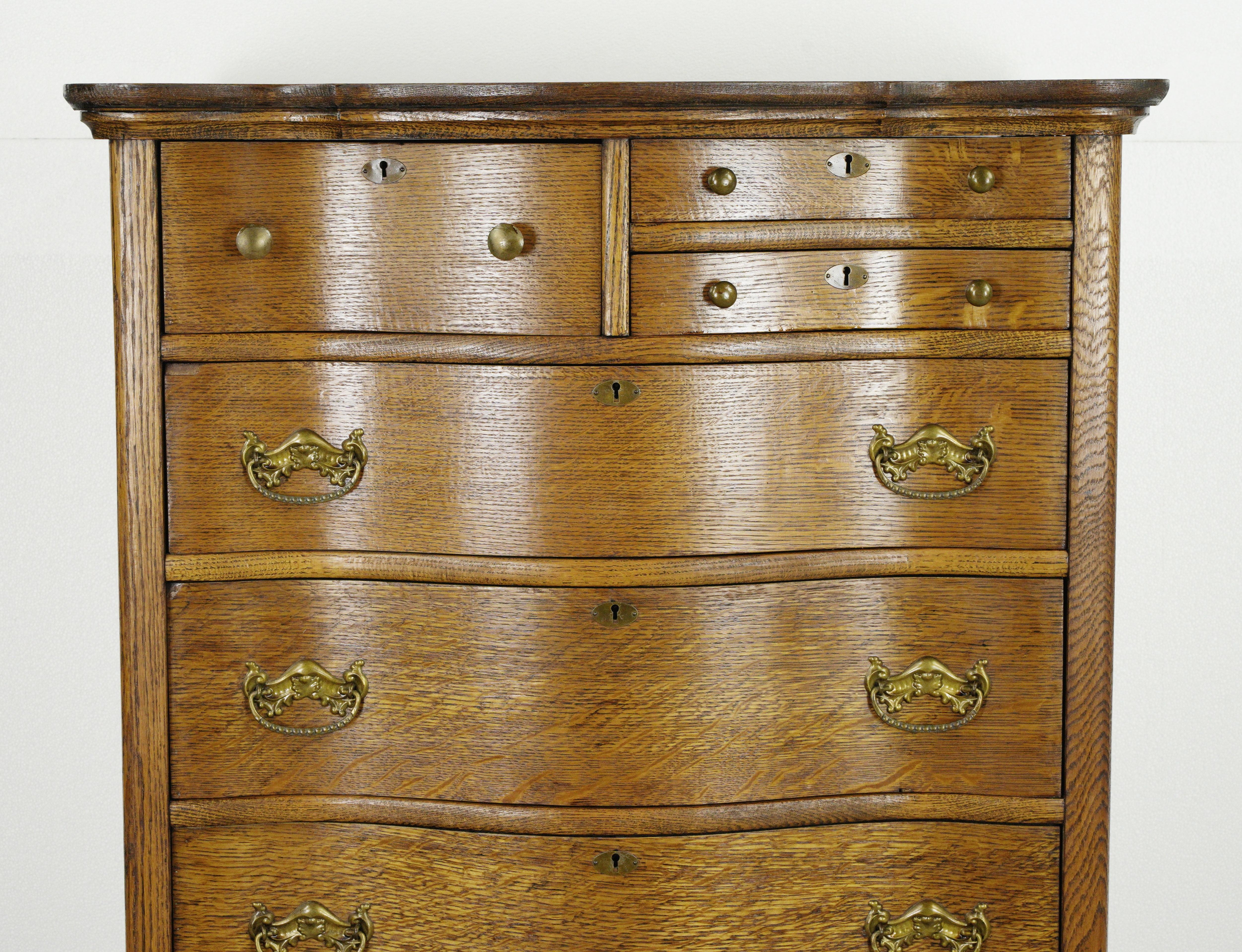 Restored antique oak serpentine front tall dresser with an unusual three upper drawer configuration and four bottom large drawers. This has all the original hardware and casters. This piece was restored in our shop. Good condition with appropriate