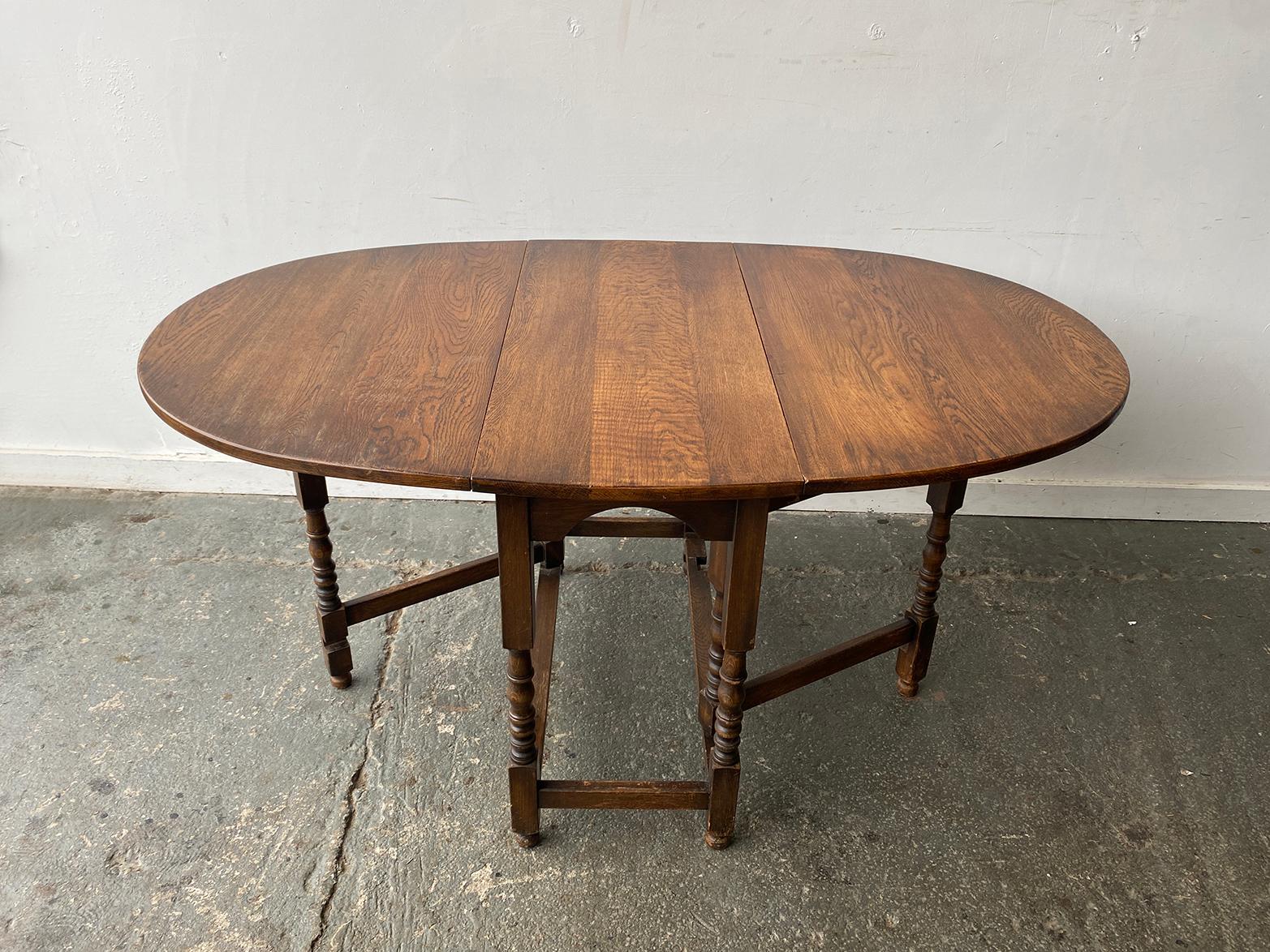 Early 20th-century oak drop-leaf gateleg table with an oval top and two hinged leaves. The table is made from solid oak with a medium-brown finish that shows the natural wood grain.

The folding leaves are supported by gate legs, allowing the table