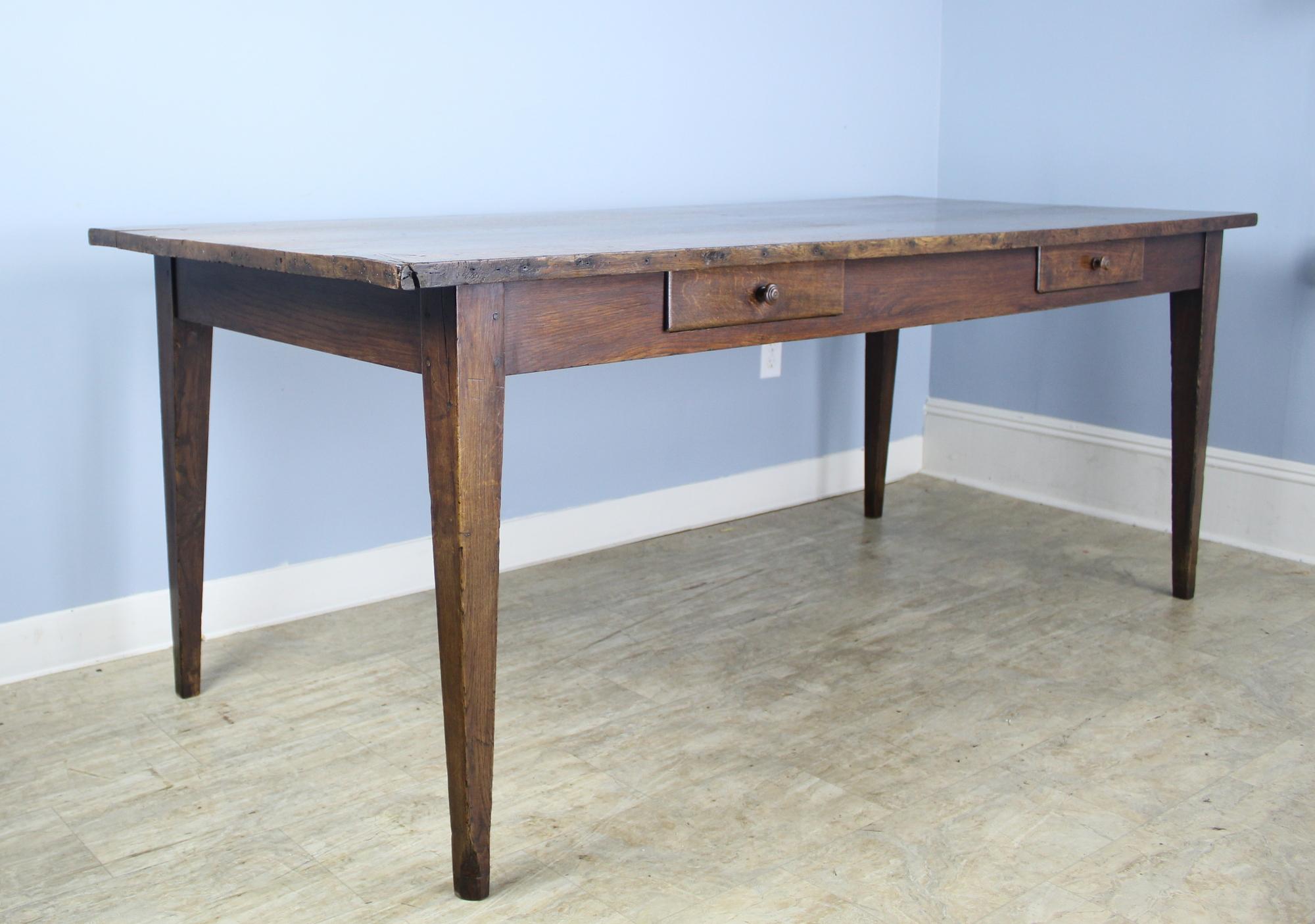 A country oak farm table with nice decorative details dramatic natural grain and knotholes and two drawers on one side. Solid and sturdy with moderately tapered legs and deep rich color and patina. Apron height is good for knees at 25