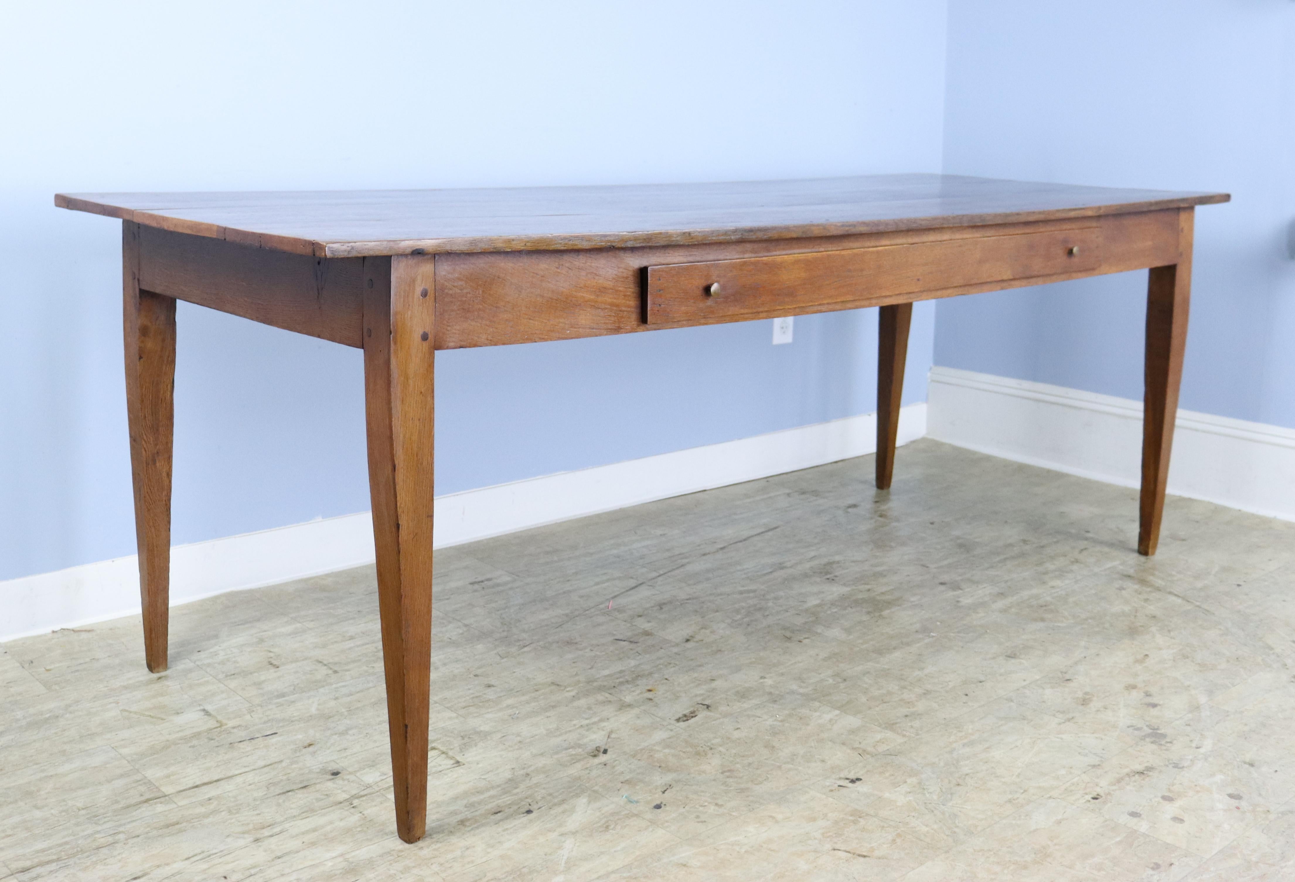 A long elegant oak farm table with an unusual long narrow single drawer. Great color and grain on the table top and classsic tapered legs, nicely pegged at the apron, which is a comfortable 24 inches. There are 71.25 inches between the legs on the