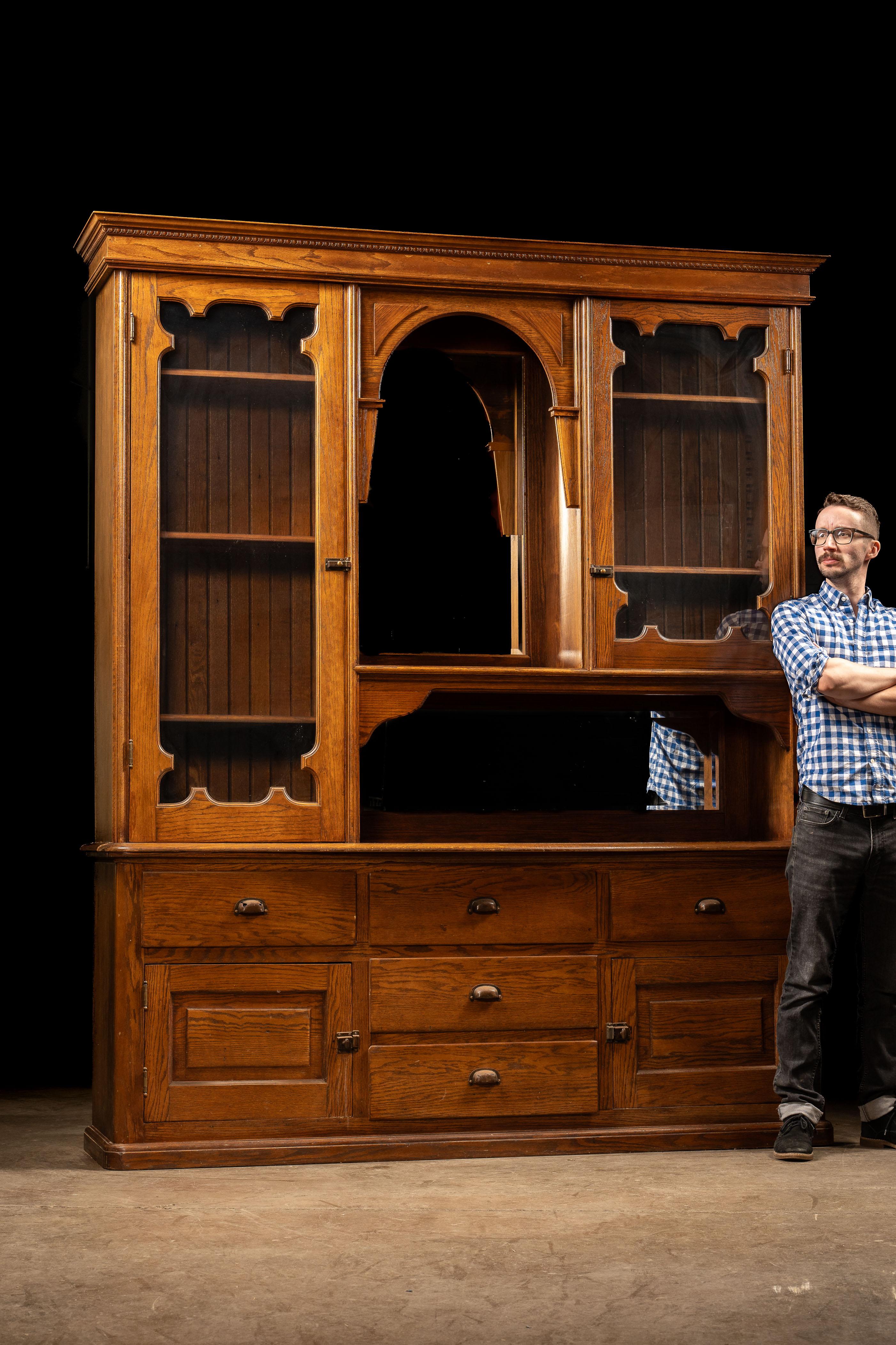 Antique wooden hutch with a mirrored back panel.

This country piece is manufactured from oak and is believed to feature all-original brass hardware. The two cabinets on either side of the central mirror boast matching styles and adjustable-height