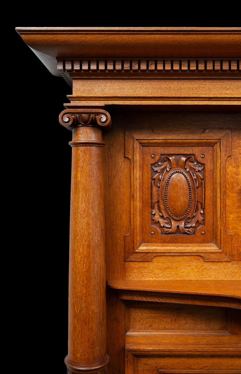 A large English antique oak fireplace from the late Victorian period.
With carved panels, dental cornice and full rounded ionic columns.

Made from a good colored oak and in great condition.


