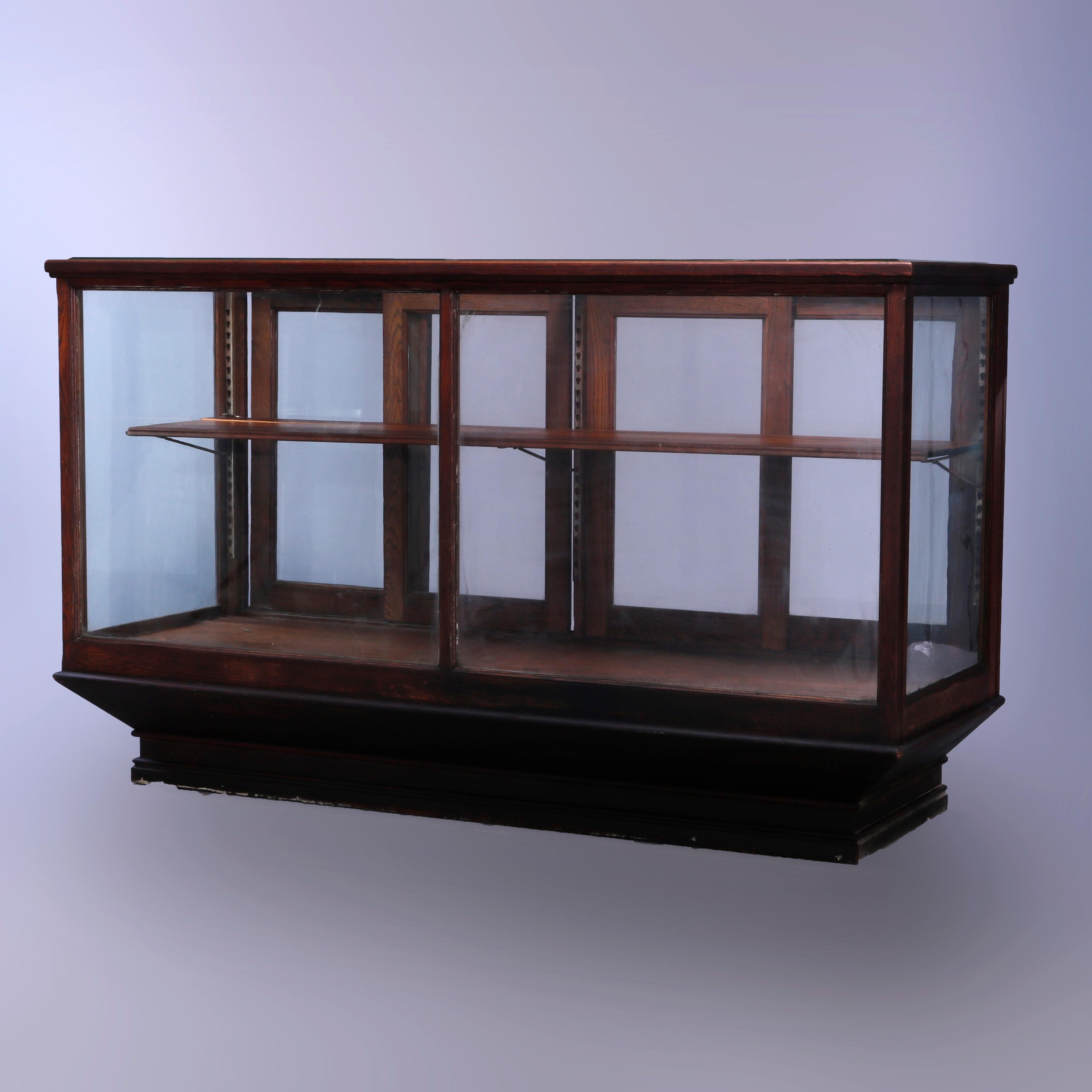 An antique country store display case offers oak construction with register counter surmounting glass case with two sets of sliding doors in back opening to shelved interior and raised on flared base, c1900

Measures - 42.5''H x 75''W x 21.75''D.