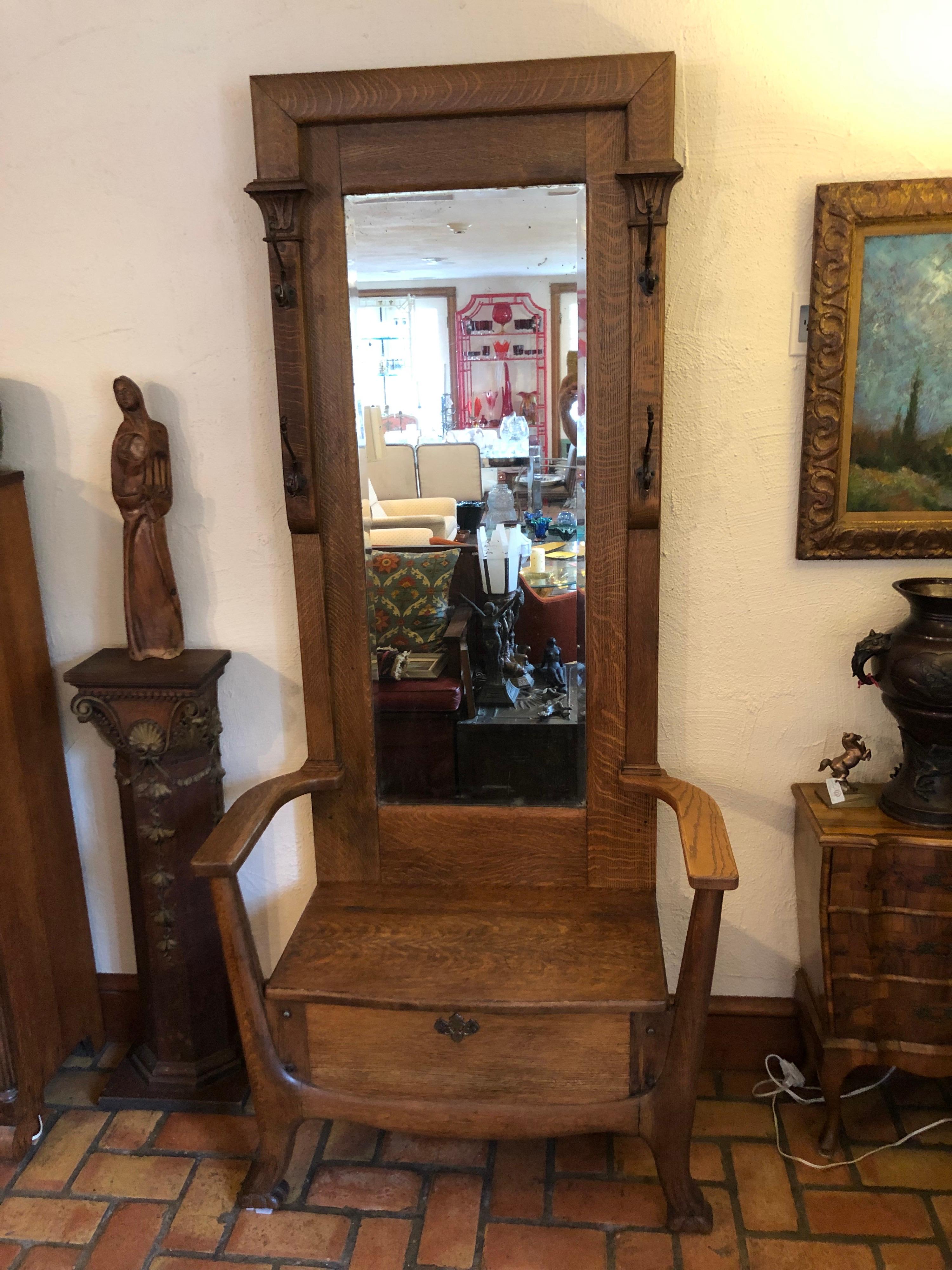 Antique oak hall tree with mirror. The perfect mudroon or front entryway piece to hold your coats, umbrellas and be able to sit down and put your boots on. Storage under seat thatlifts up. Four hooks and the original beveled mercury glass mirror.