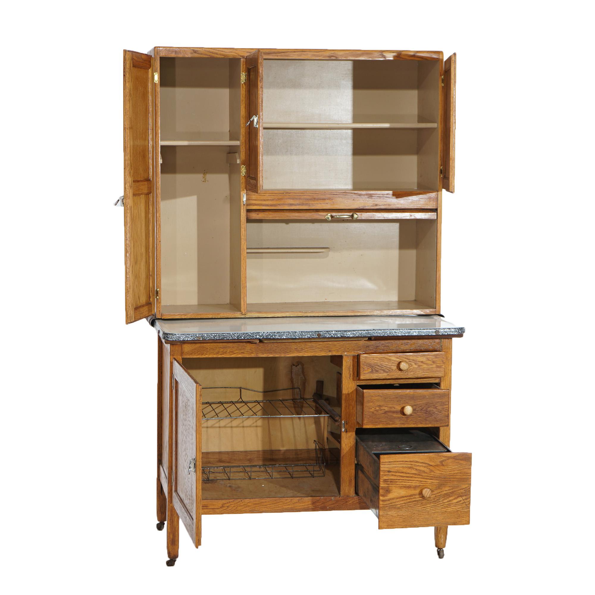 An antique Hoosier kitchen cabinet offers oak construction with enameled metal pull-out work surface, c1920

Measures- 69.75''H x 42.25''W x 25.5''D