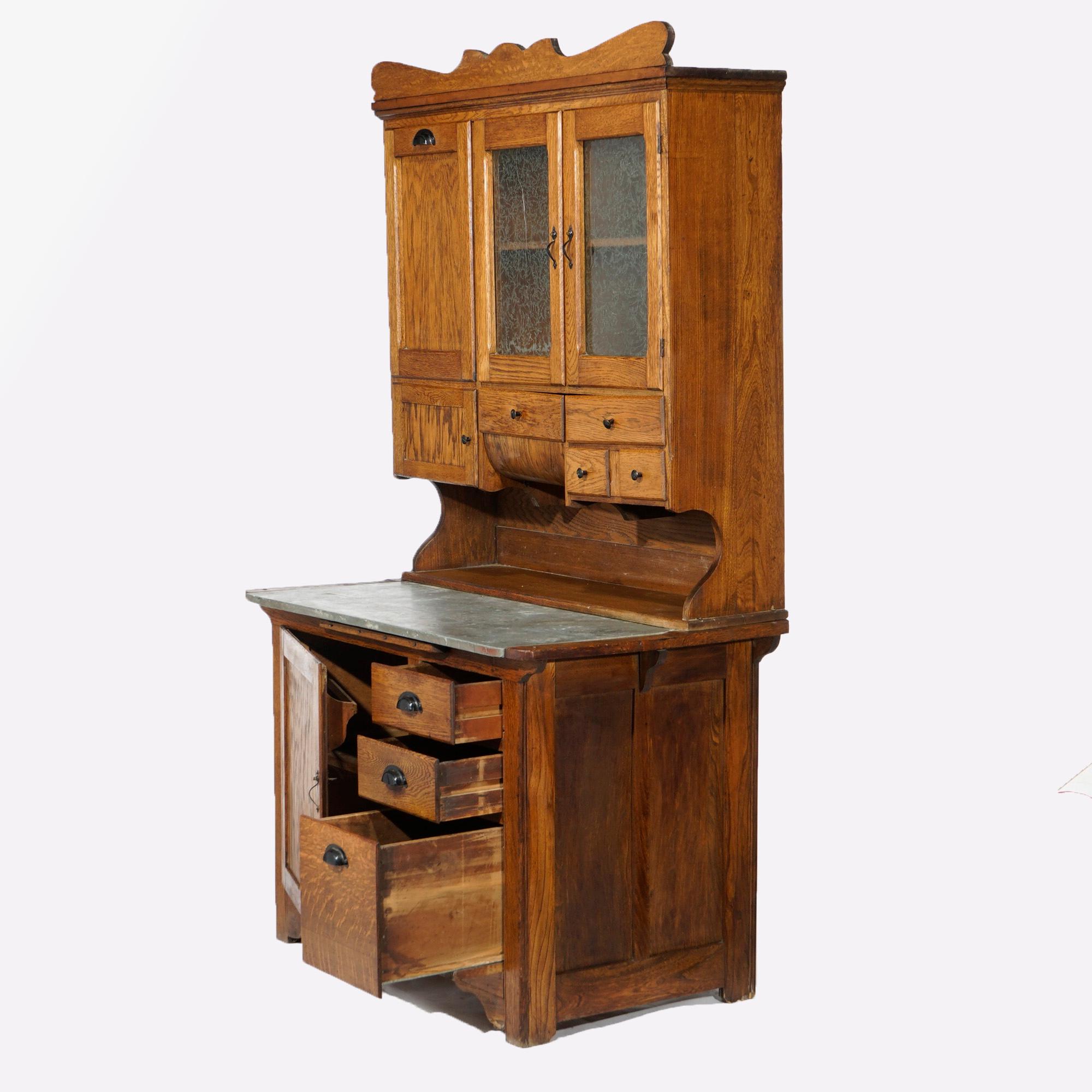 An antique Hoosier kitchen cabinet offers oak construction with shaped crest over upper with pull out flor bin and cabinets over work space having lower cabinets, c1900

Measures- 75.75''H x 42.5''W x 26.5''D
