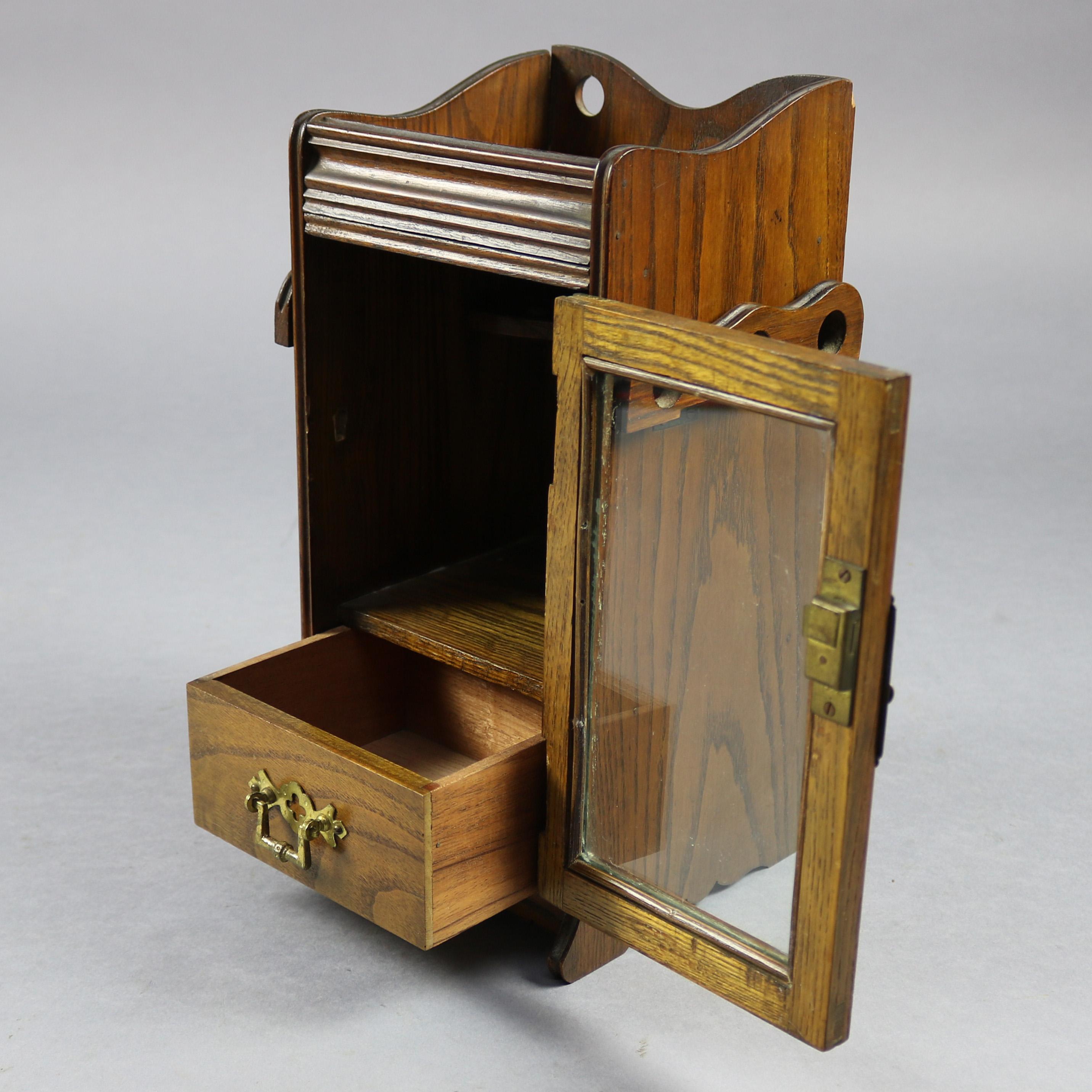 An antique humidor and display offers oak construction with single glass front door opening to reveal an internal storage compartment and lower drawer, sides having fold down pipe racks, circa 1890

Measures: 12.75