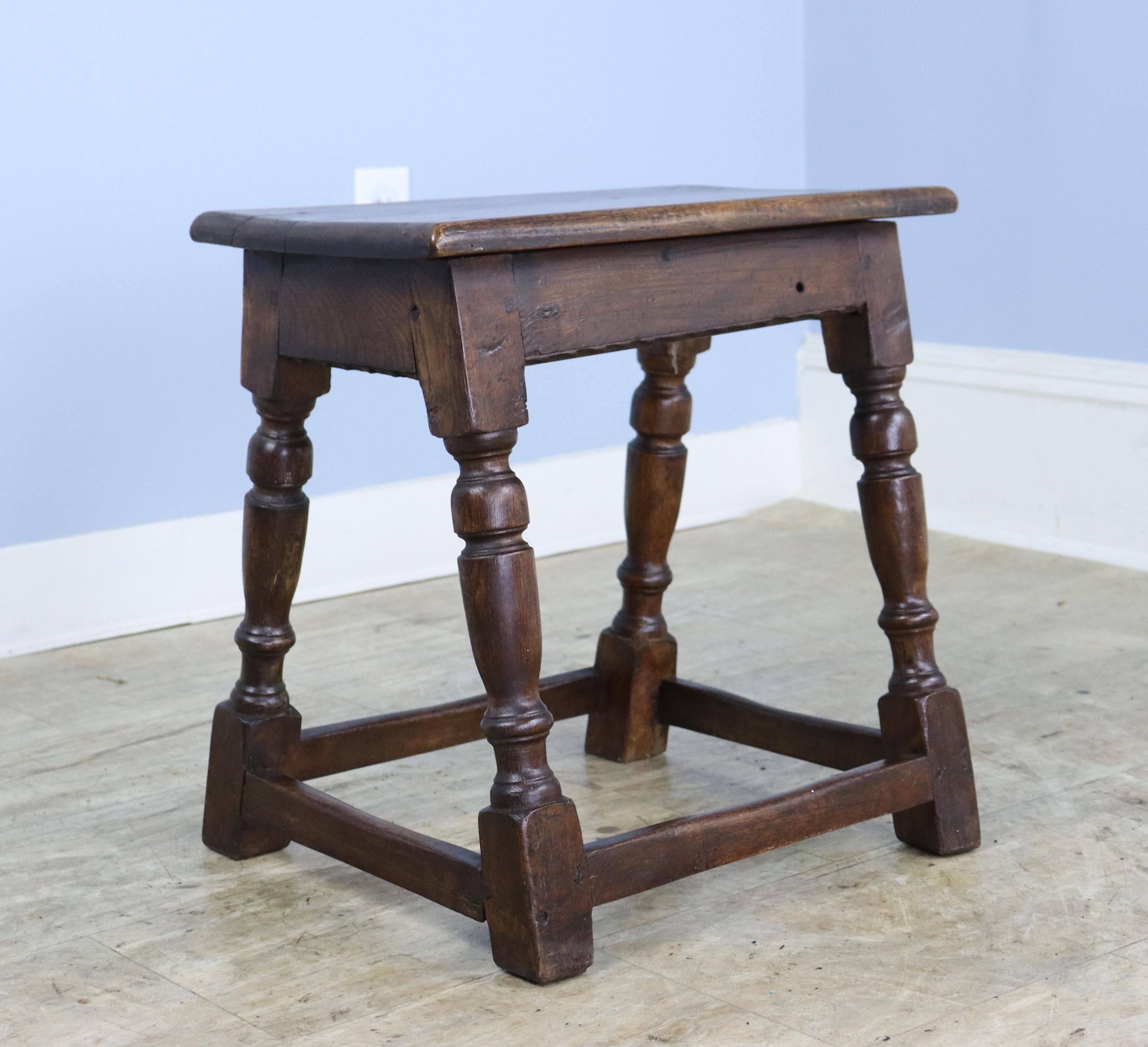 A long carved oak footstool, chunky and handsome. The turned legs add an additional design note. Perfect as a fireside perch or at the end of a guest bed. There is a small hole in the apron of the seat, visible in thumbnails.