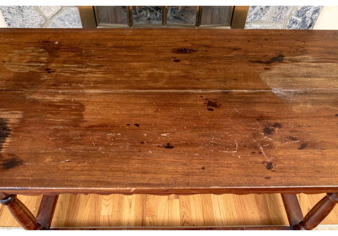 A wonderful antique library table in medium brown finished oak. With a carved apron and two drawers adorned with knob pulls to one side on four turned legs with stretcher supports. Features a wide rectangular top and a long and short drawer adorned
