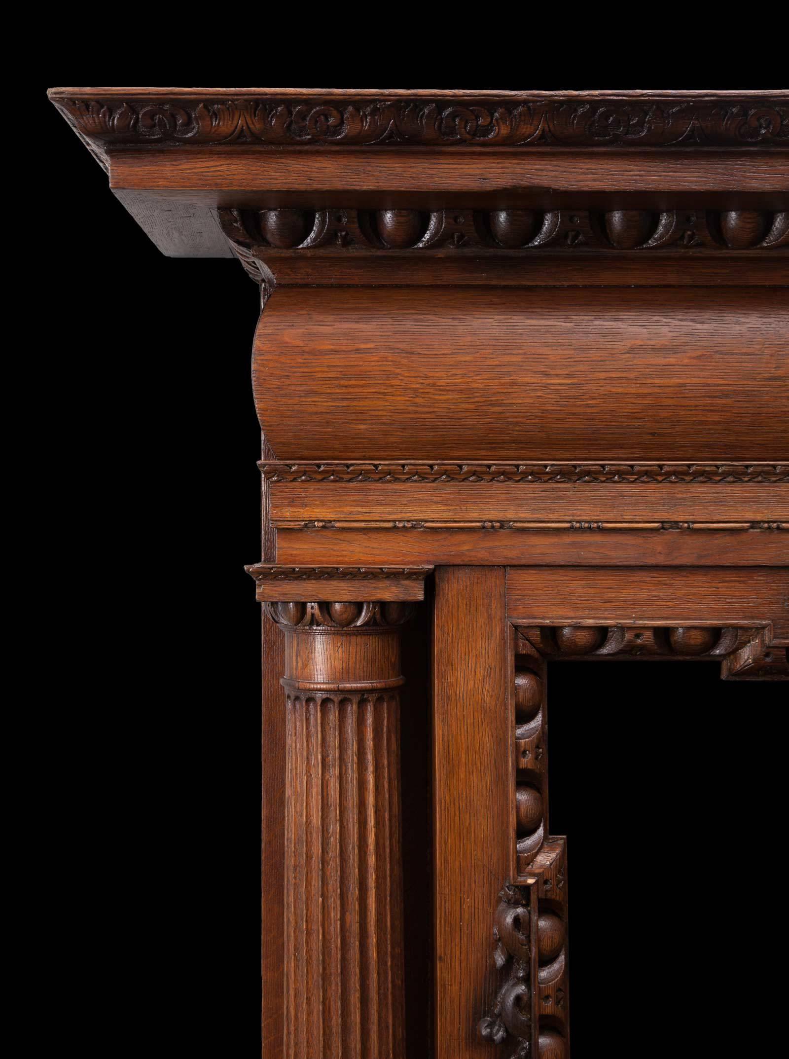 A large antique English carved oak mantelpiece in the Palladian style. With full rounded and fluted Doric columns, egg and dart mouldings and a carved floral centre tablet. Beautifully made during the Victorian period, from a wonderful coloured oak.
