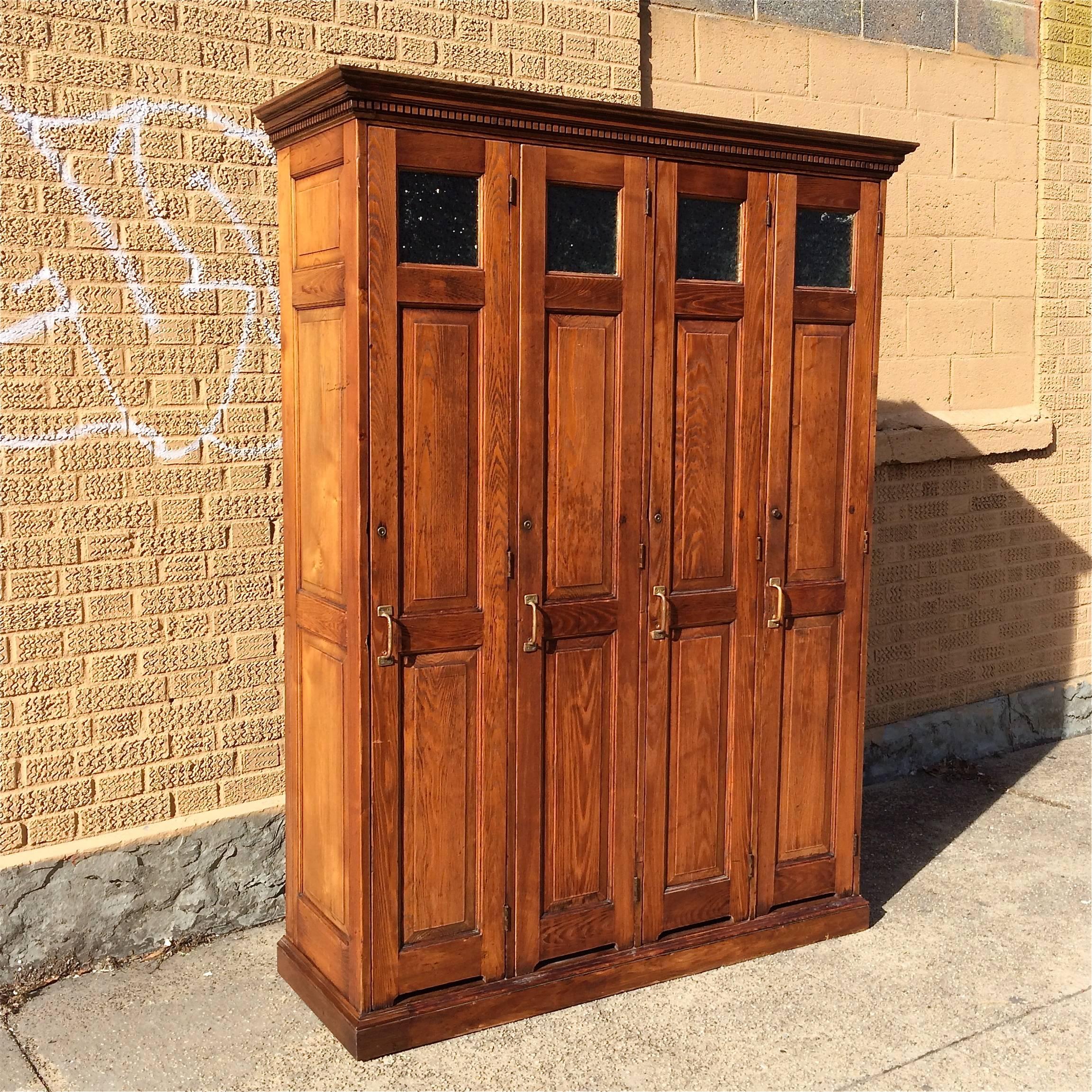 Row of four, antique, late 19th century, oak, police lockers with brass handles and textured glass windows. Locker interiors are painted black. 52.25