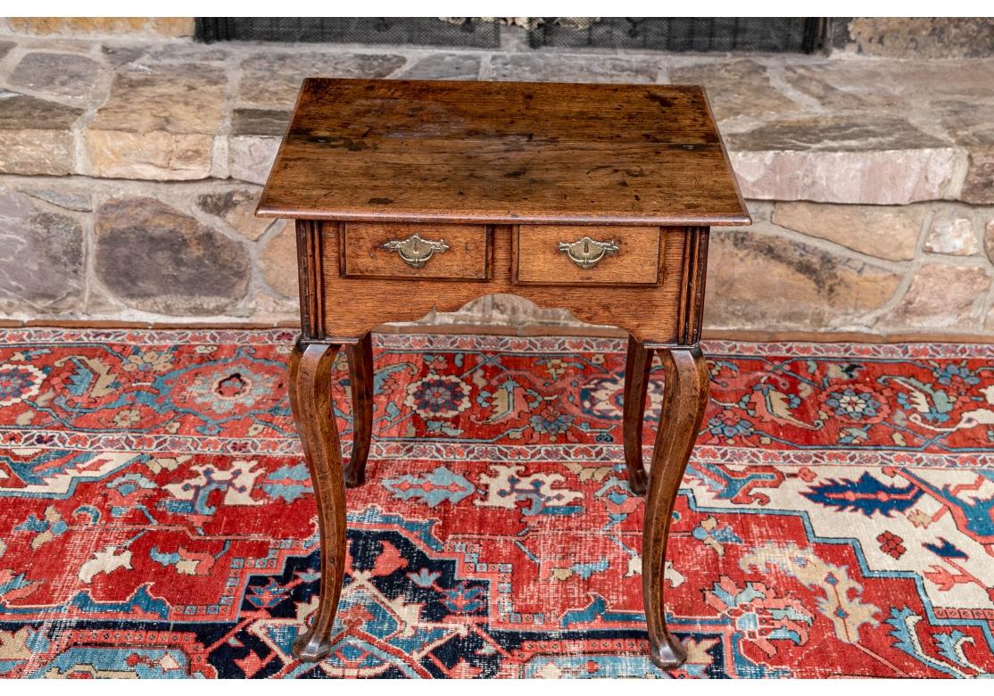 A very well made Antique Solid Oak side table in the Queen Anne style in original condition with a classic English Oak stain. The table with double drawers having incised brass brass batwing pulls and the case, with carved apron resting on tall