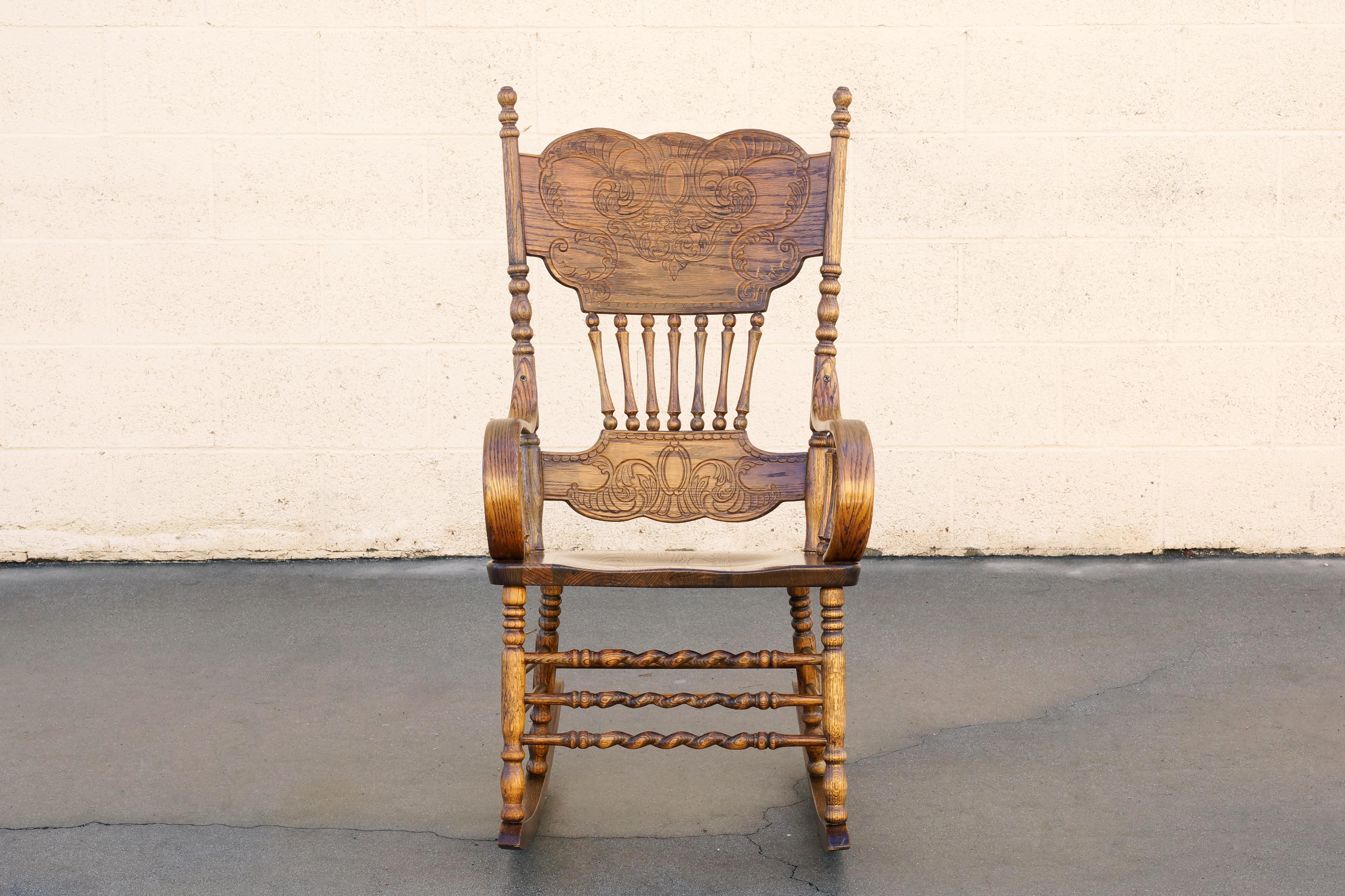 Vintage, antique-style oak rocking chair with wonderful press back design. This beautifully crafted seat also features thick bentwood arms, spindles and twisted wood accents. In excellent condition with a reconditioned golden oak patina. c. 1970s/