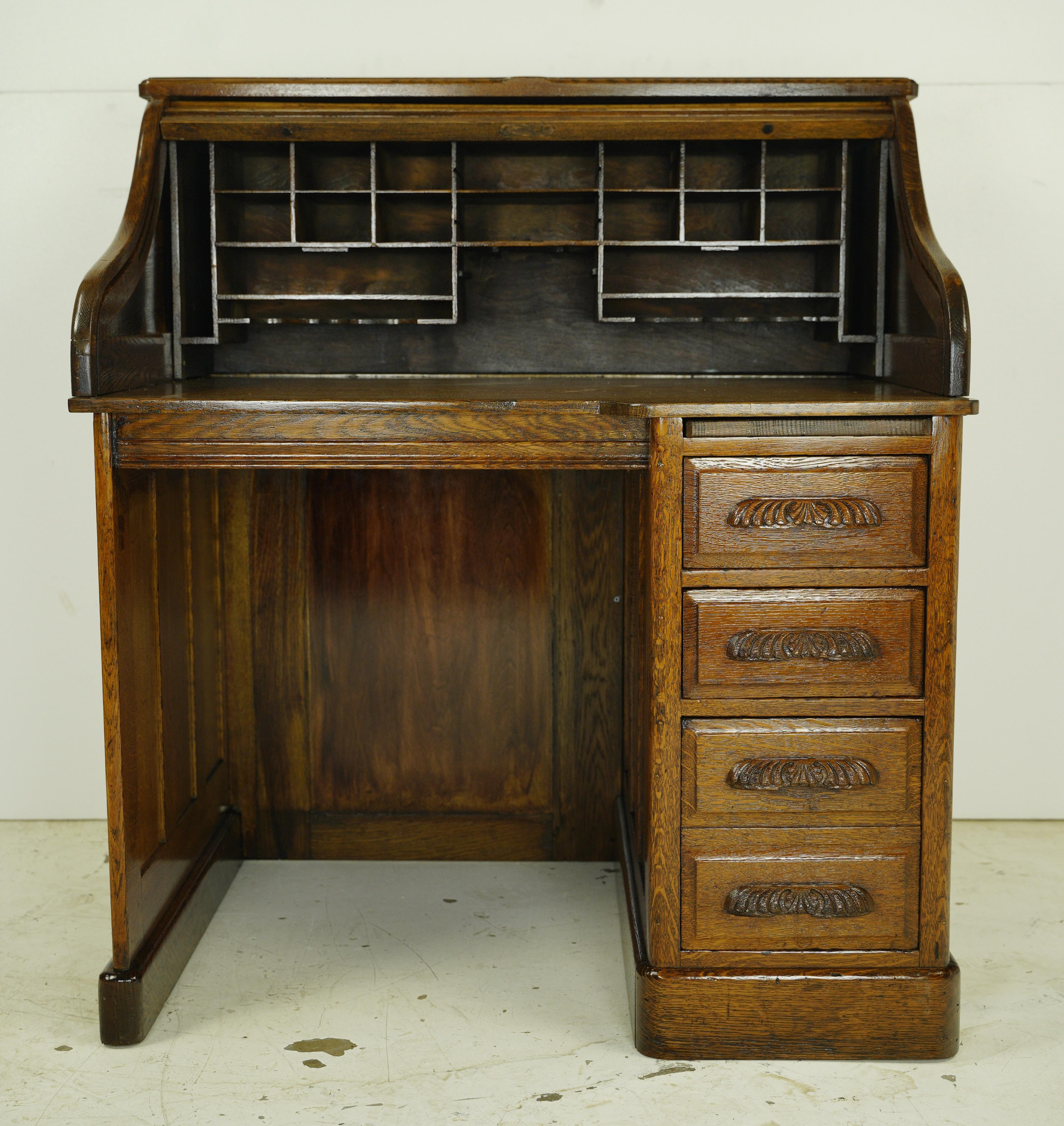 This antique right-hand pedestal roll top desk features dovetailed drawers, 20 desktop compartments, a pull out tabletop and wood scalloped drawer pulls. Good condition with surface wear from age and prior use. One available. Please note, this item