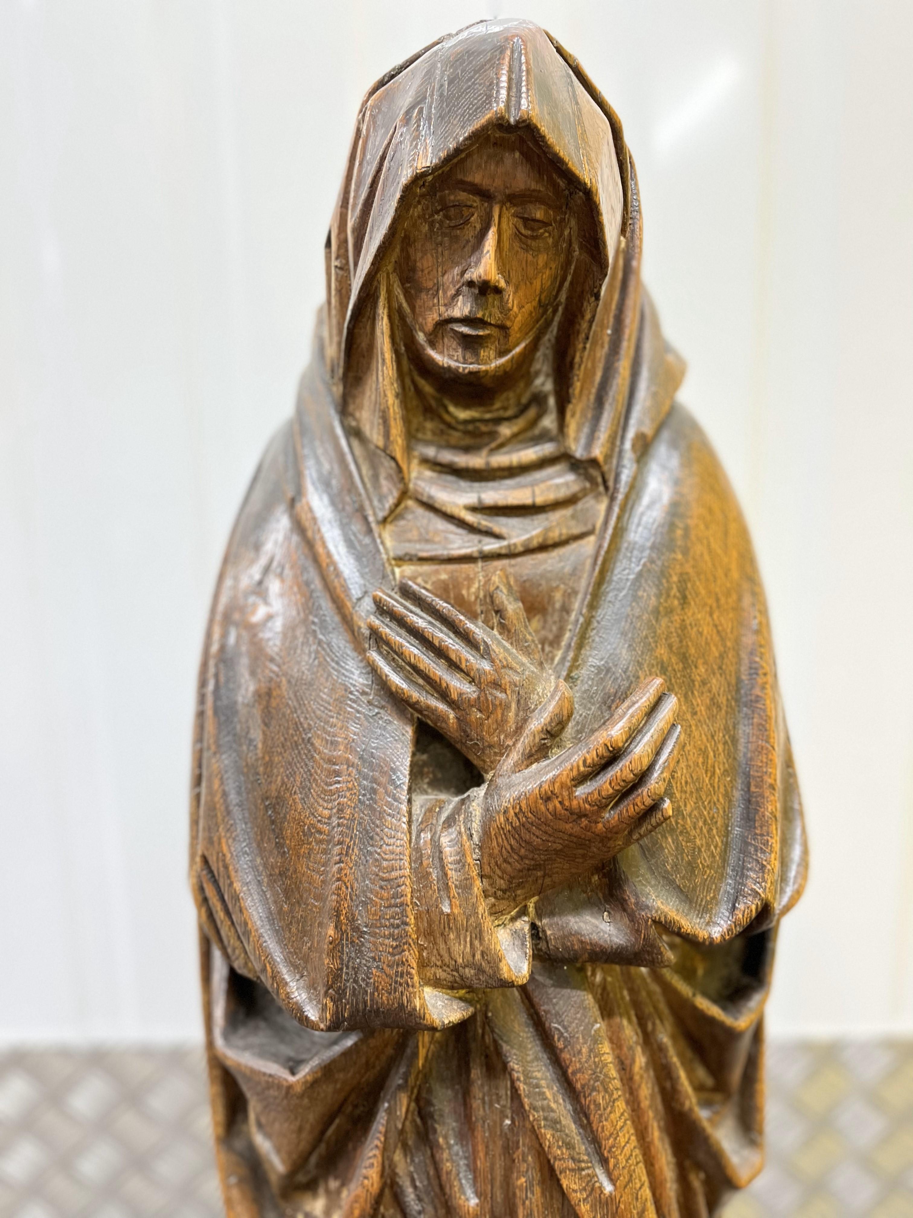 A Late 15th/Early 16th Century Oak Sculpture depicting ‘The Grief of Mary’, carved almost in the round with Mary wearing a head scarf, neckerchief and draped mantle over a long tunic, her hands crossed over her breast, mounted on a moulded hexagonal