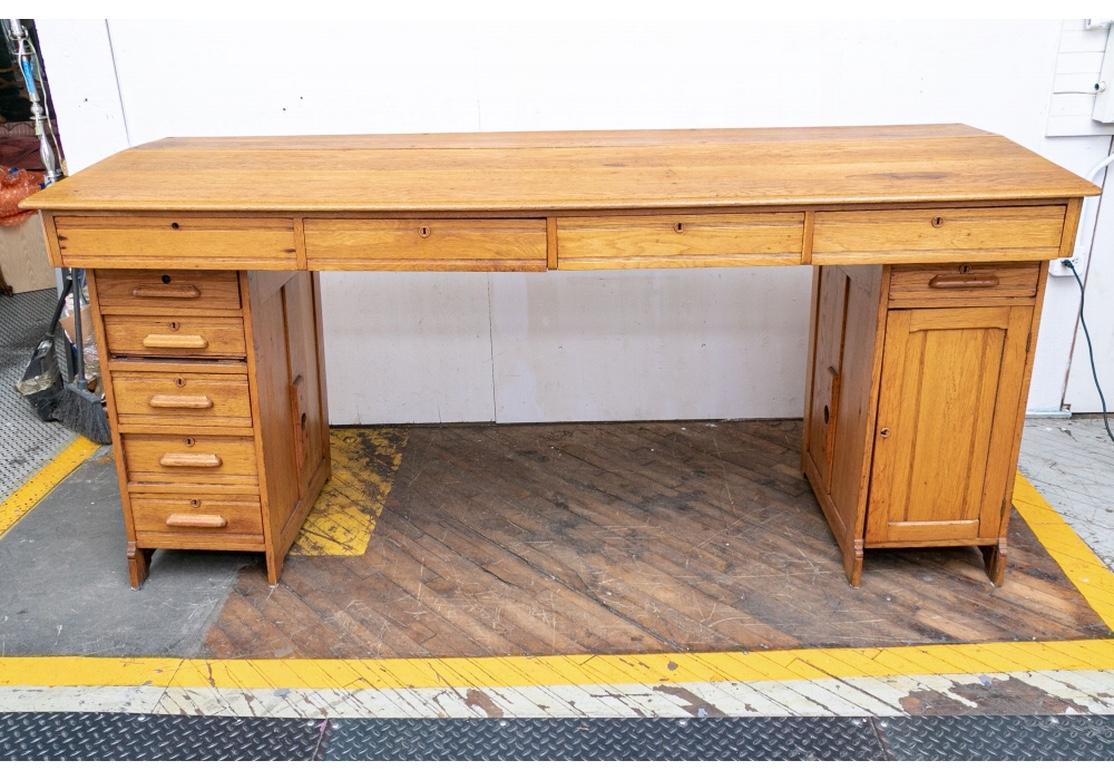 A very good condition and quite large antique oak shop counter with four top drawers and two pedestals, one having an additional five wood-handled drawers and the other with one top drawer and a door opening to reveal slotted compartments and cubby