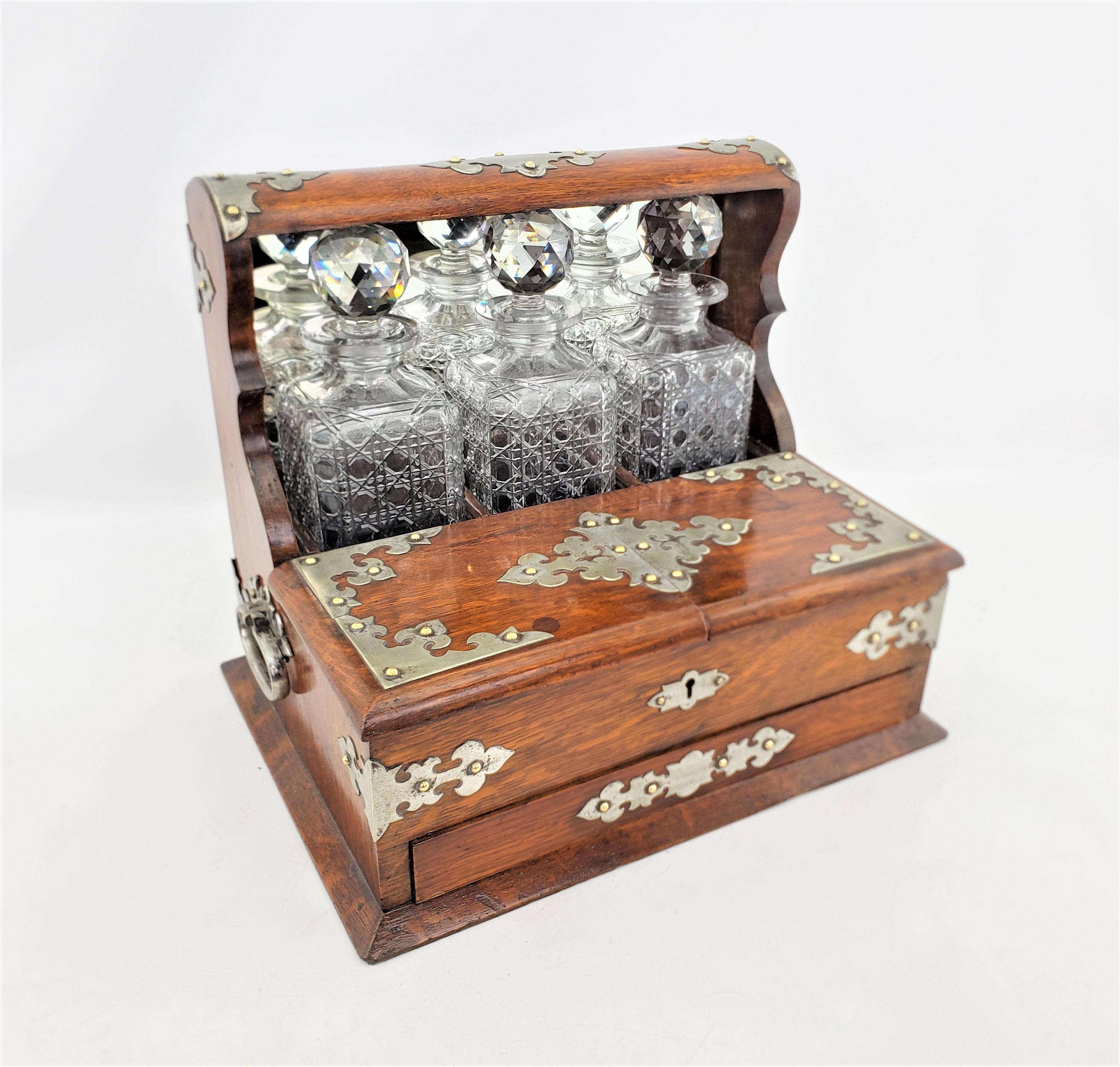 This antique tantalus is unsigned, but presumed to have originated from England and date to approximately 1880 and done in the period Victorian style. The tantalus with composed of oak with elaborate pierced and silver plated mounts, with three cut