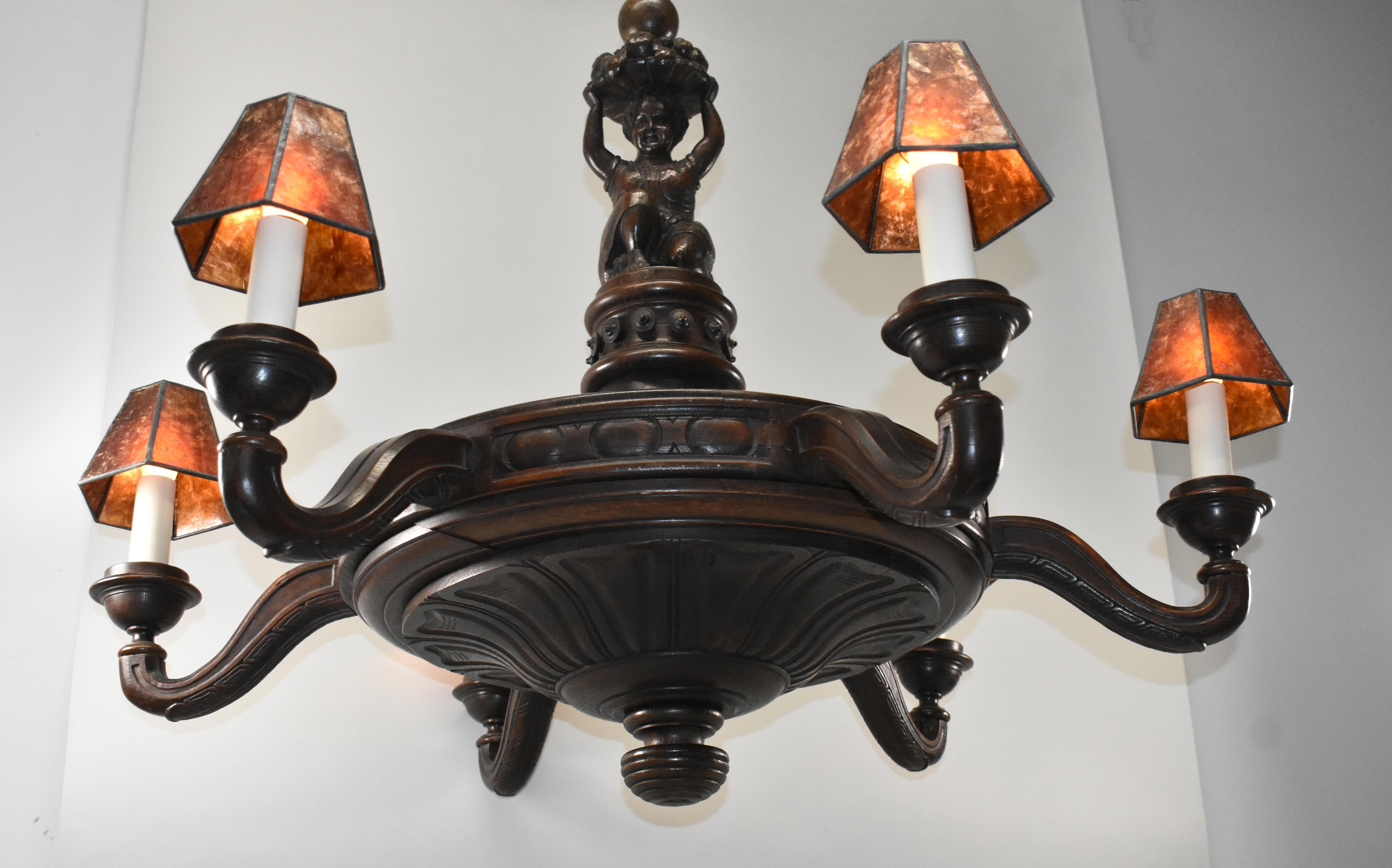 Antique oak large scale tavern, pub or wine cellar chandelier circa 1920s. Original finish. Hand carved full figure of a child holding a basket in center. Six carved arms that hold mica shades. Has been rewired. Dimensions: 32