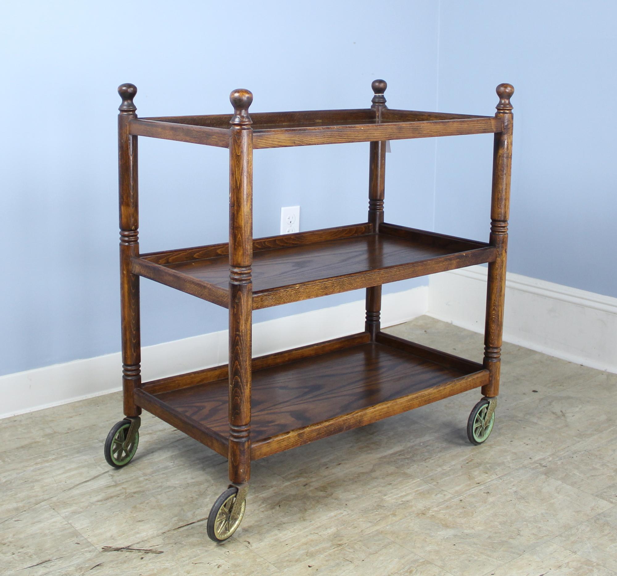 Charming three-tier bar cart. Rich dark oak, with decorative turned legs with small rounded tops. Original castors. There are 11