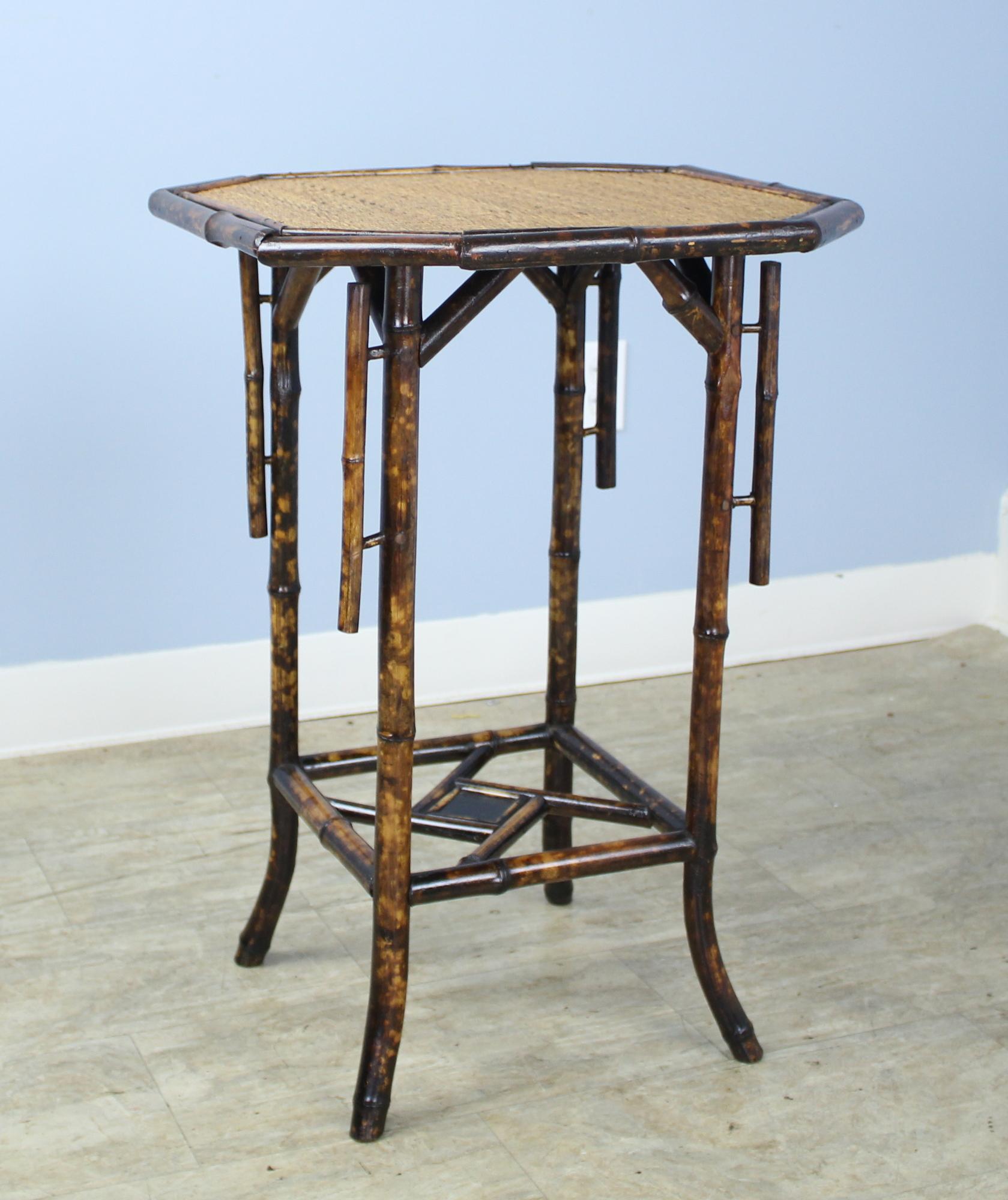 An antique English bamboo side table, with flared legs and with and an unusual octagonal top accented with vertical detail. The top shelf is made of tightly woven rattan that is in very good condition. The bottom has a stylish bamboo configuration.