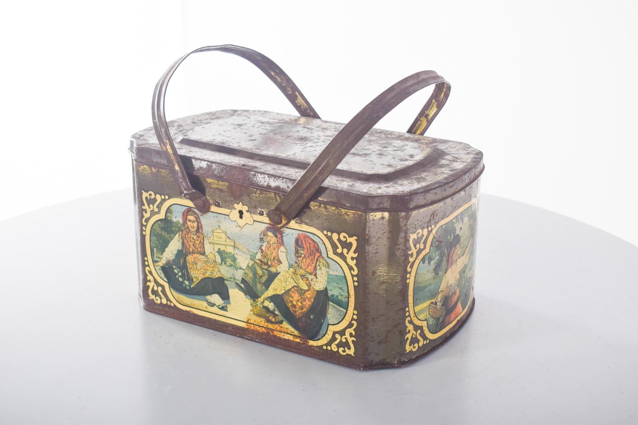 Caja de latón antiguo. De forma rectangular, con tapa abatible y dos asas móviles, evoca el estilo de las fiambreras de los años 40-50. Decoración litografiada en todas las caras, con coloridos grabados que representan figuras con trajes