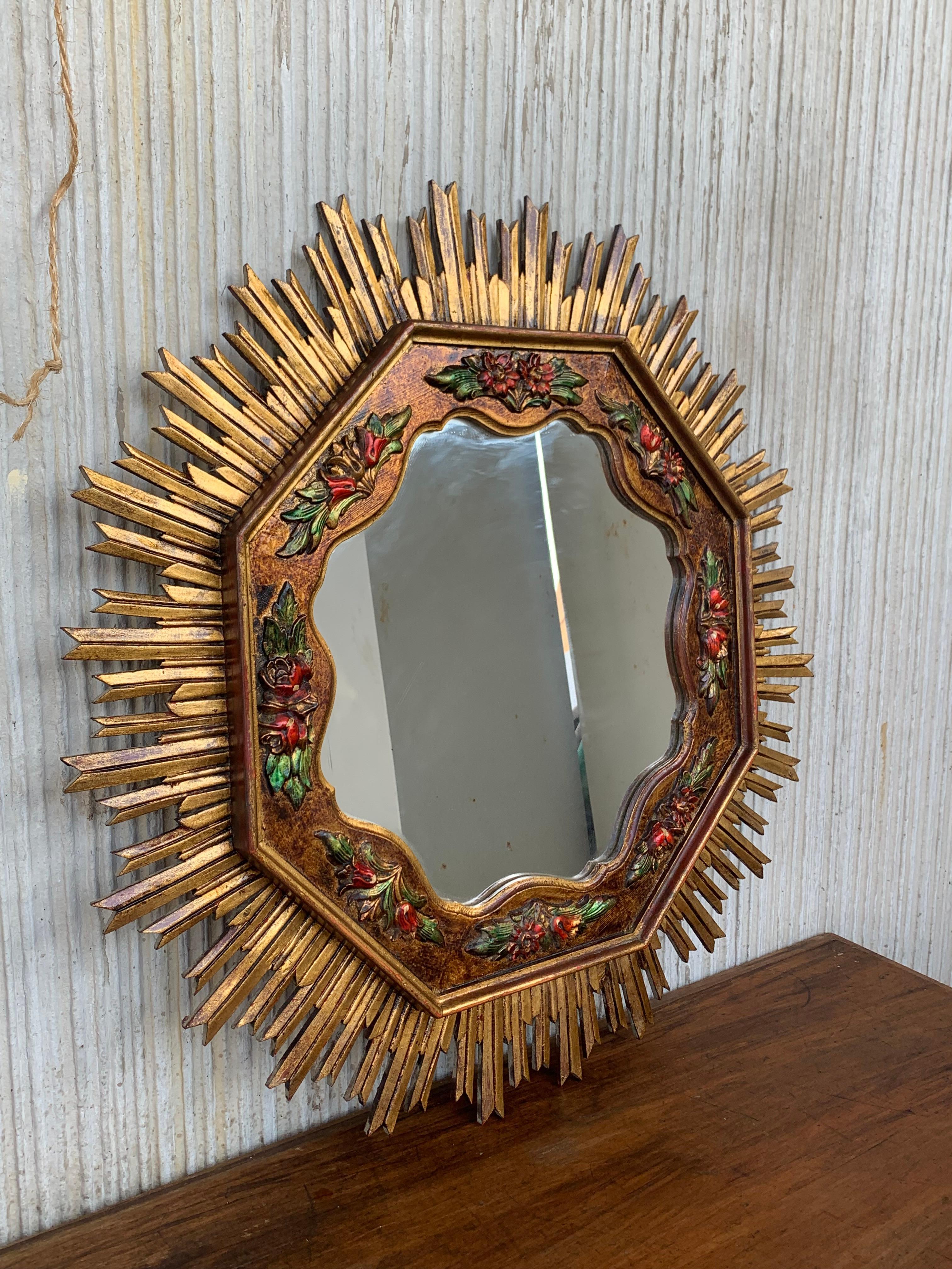 A magnificent and large early to mid-20th century French gilded and carved wood sunburst mirror with unusual octogonal shape, featuring a beautiful carved and highly decorative wood polychrome barbola wreath of flowers – which was a trend in the