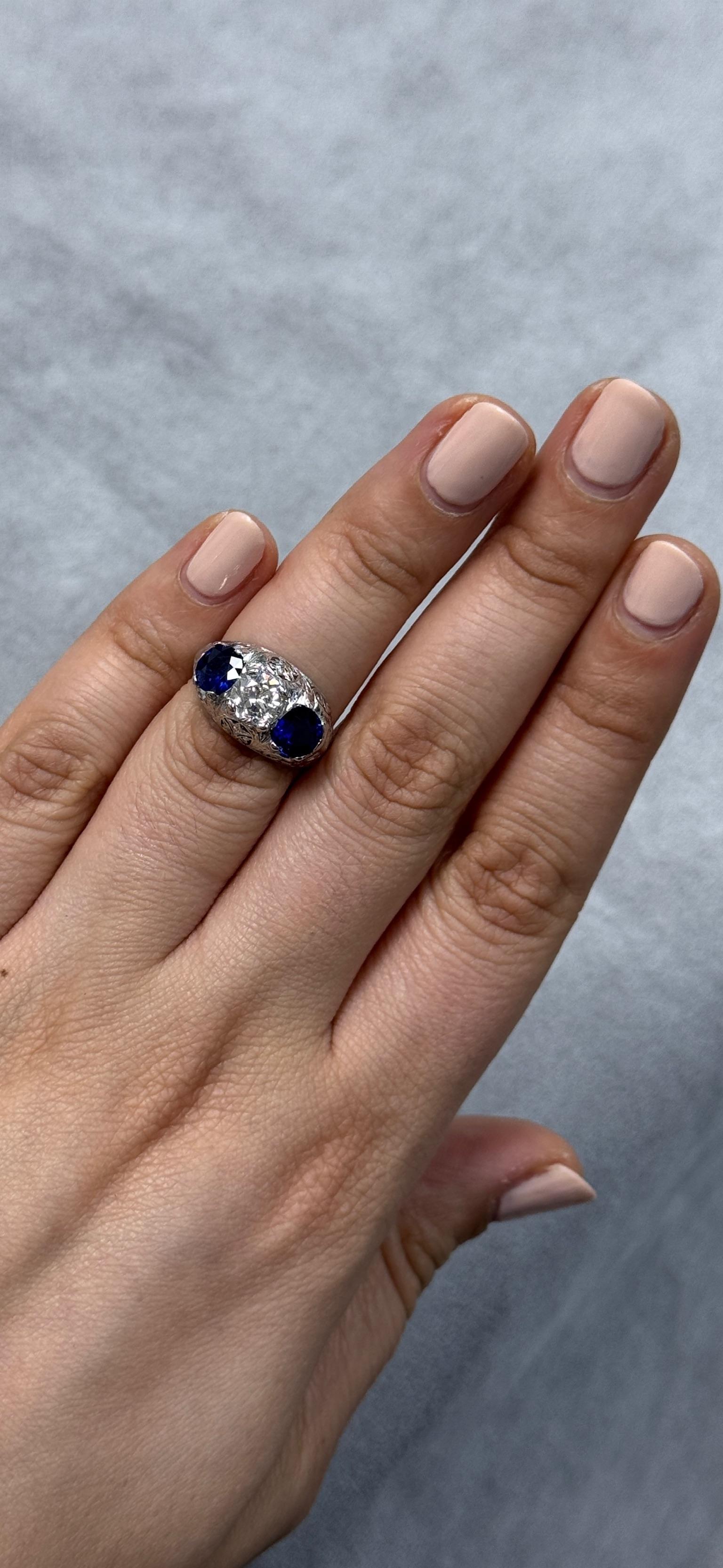 Questo antico anello trilogy presenta uno splendido diamante di 1,00ct con taglio Old European (colore I-J, purezza VS) affiancato da 2,00ct di vibranti zaffiri naturali. Gli intricati dettagli in filigrana di platino aggiungono un tocco di arte