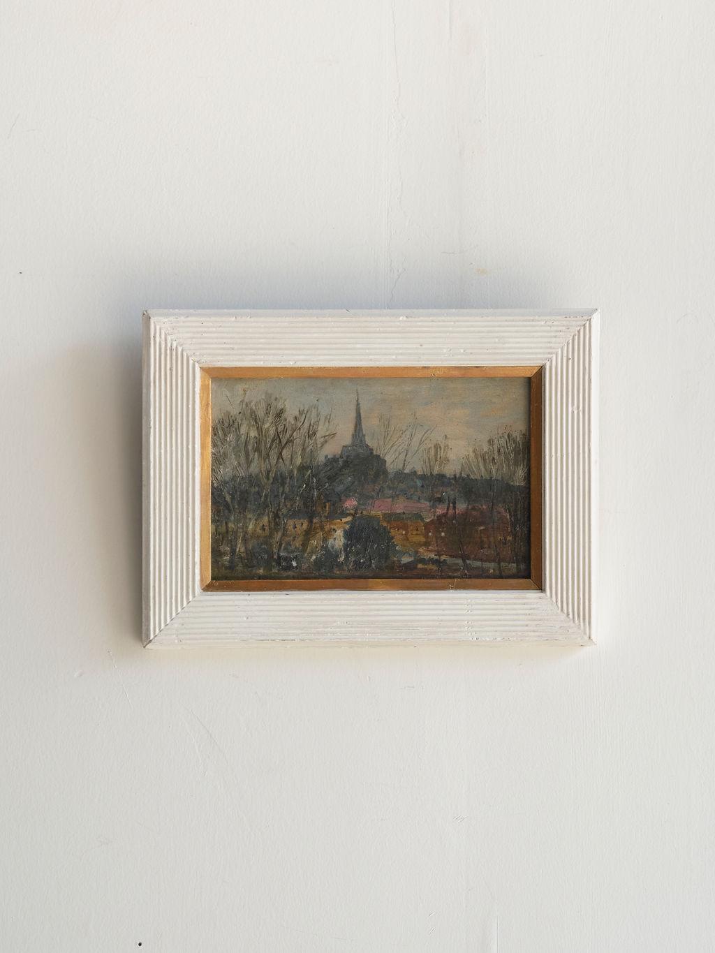 A lovely 20th century oil painting of an English landscape with a church in the background. The contrast of the muted colors of the painting and the bright white frame really make this piece of art stand out. The frame has white ribs on every side