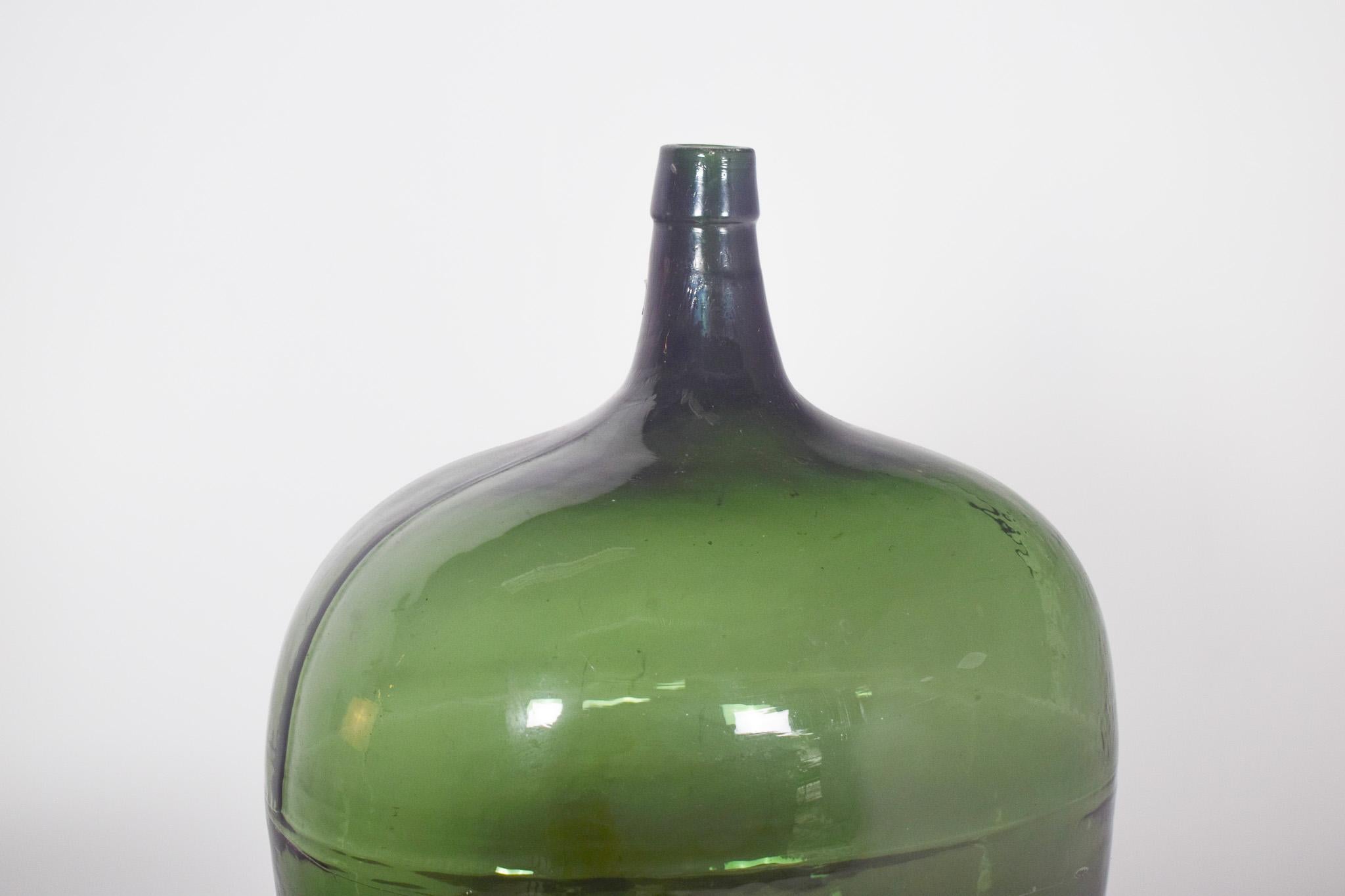 Vieille bouteille, en verre vert. Verre vert foncé, rond et à col étroit, adapté au stockage de liquides tels que le vin, l'huile ou l'eau.
Le verre présente quelques irrégularités, typiques du processus de fabrication artisanale, et la surface est